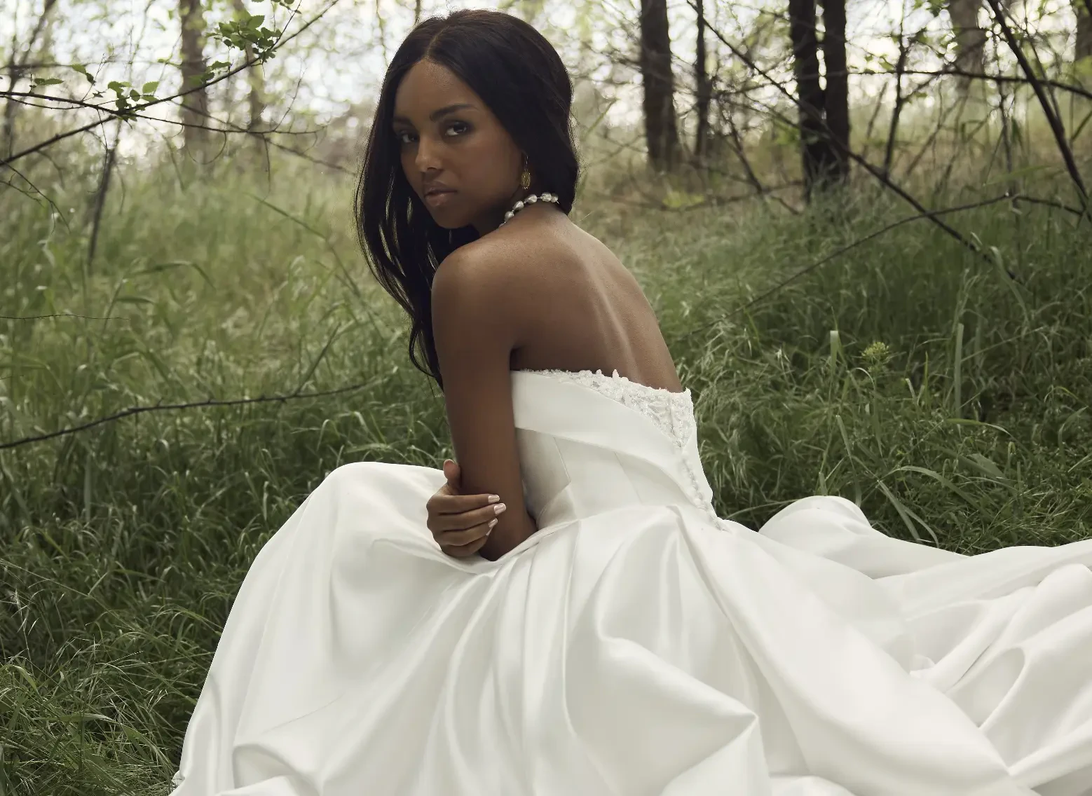 Model Wearing Satin Wedding Dress Called Agatha By Rebecca Ingram Sitting In Grass