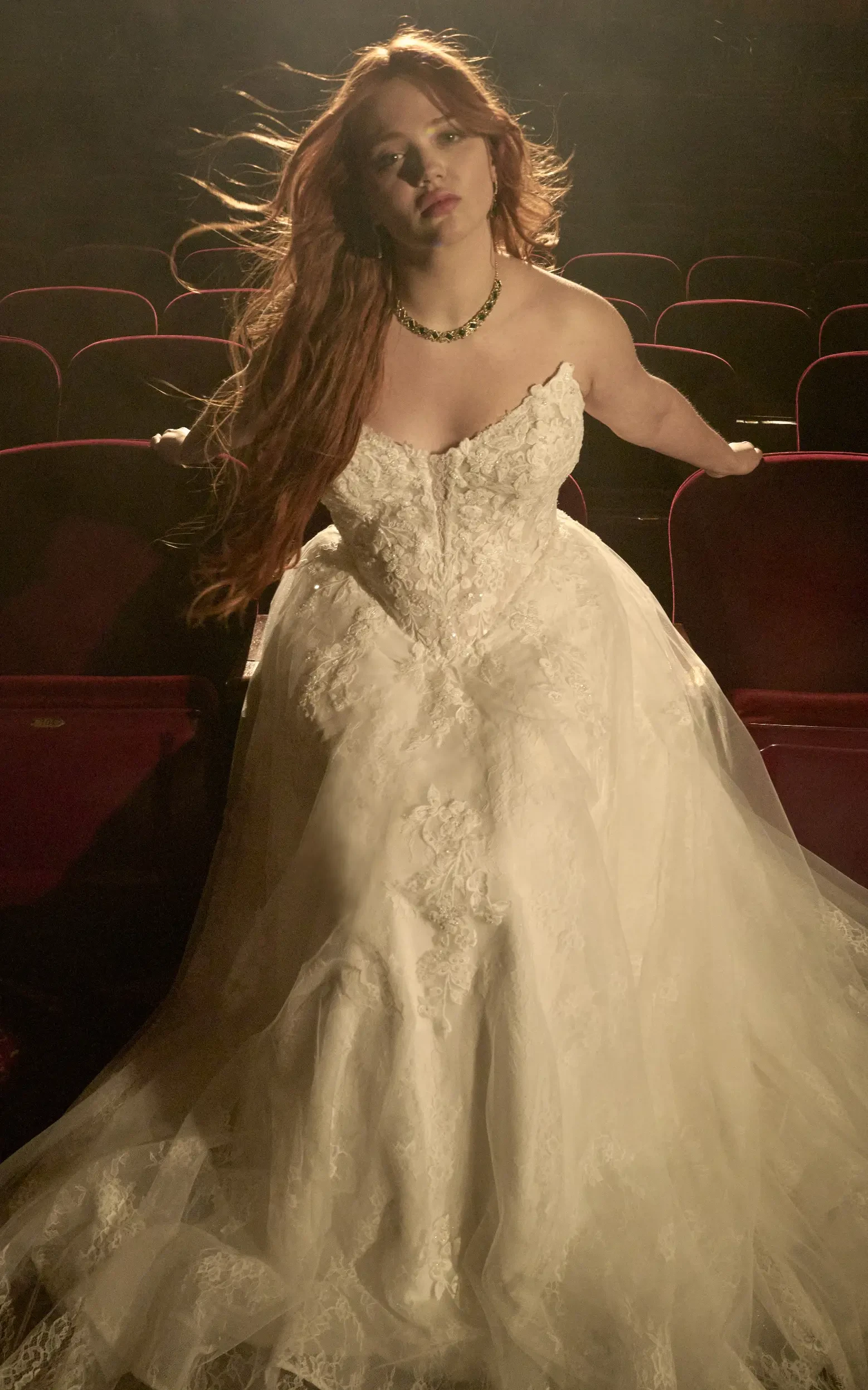 Model Sitting In Theater Seats Wearing Off-white Wedding Dress Called Hadley By Maggie Sottero