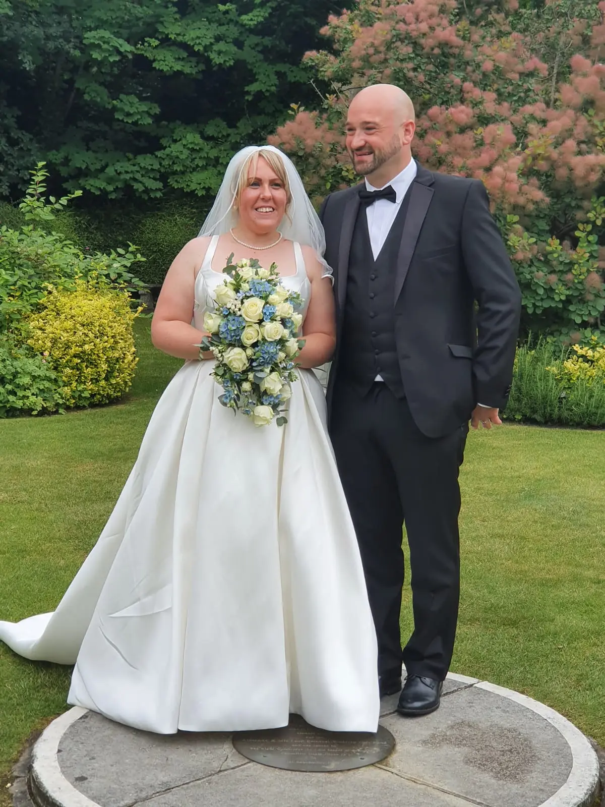 Bride and groom smiling in a well-kept garden.