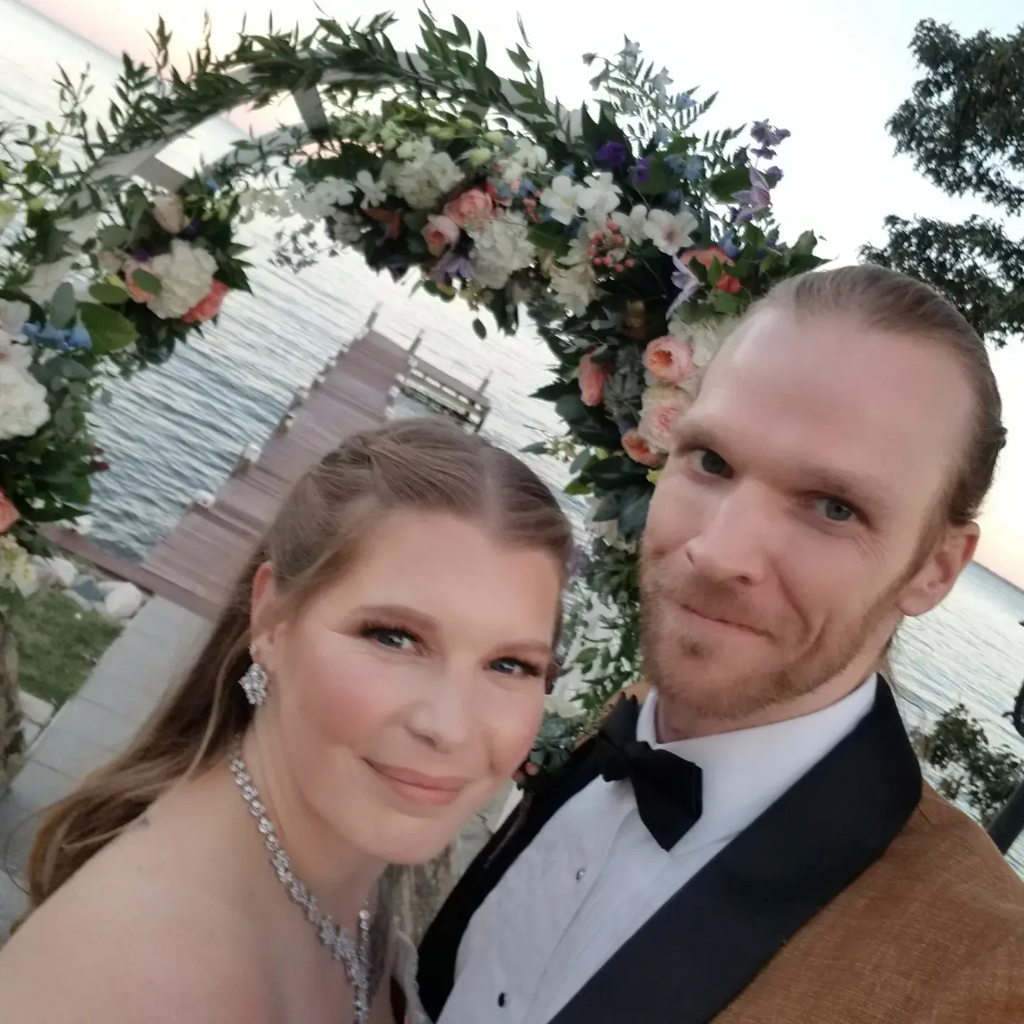 Bride Wearing Princess Wedding Dress With Long Sleeves Called Stevie By Maggie Sottero Selfie With Groom Under Floral Arch