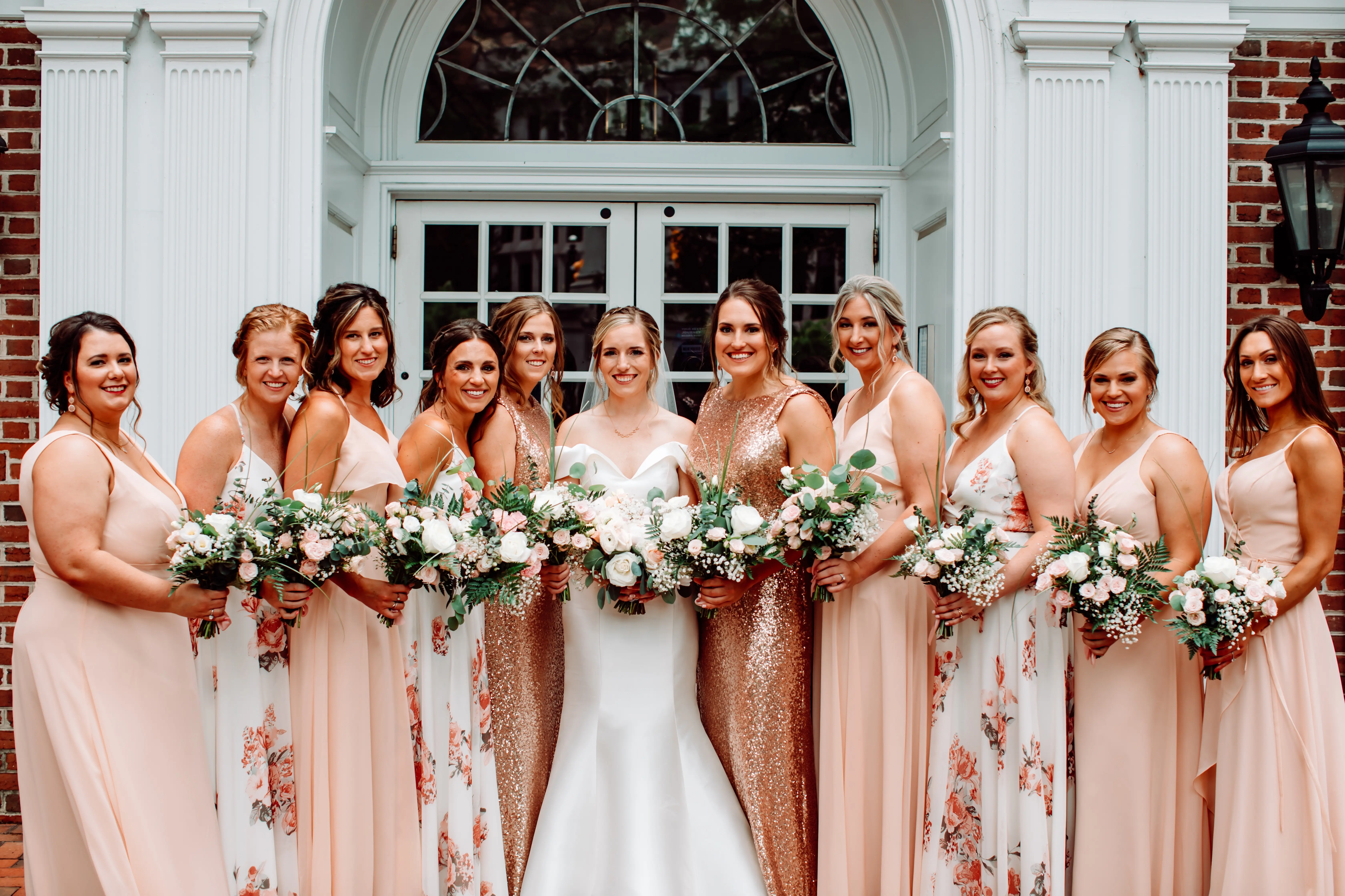 Bride with her bridesmaids wearing mix and match dresses in tones of rose gold, light blush and coral.