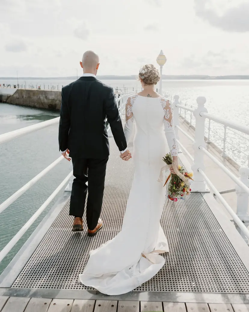 Bride wearing Bethany wedding dress by Rebecca Ingram walking with her husband