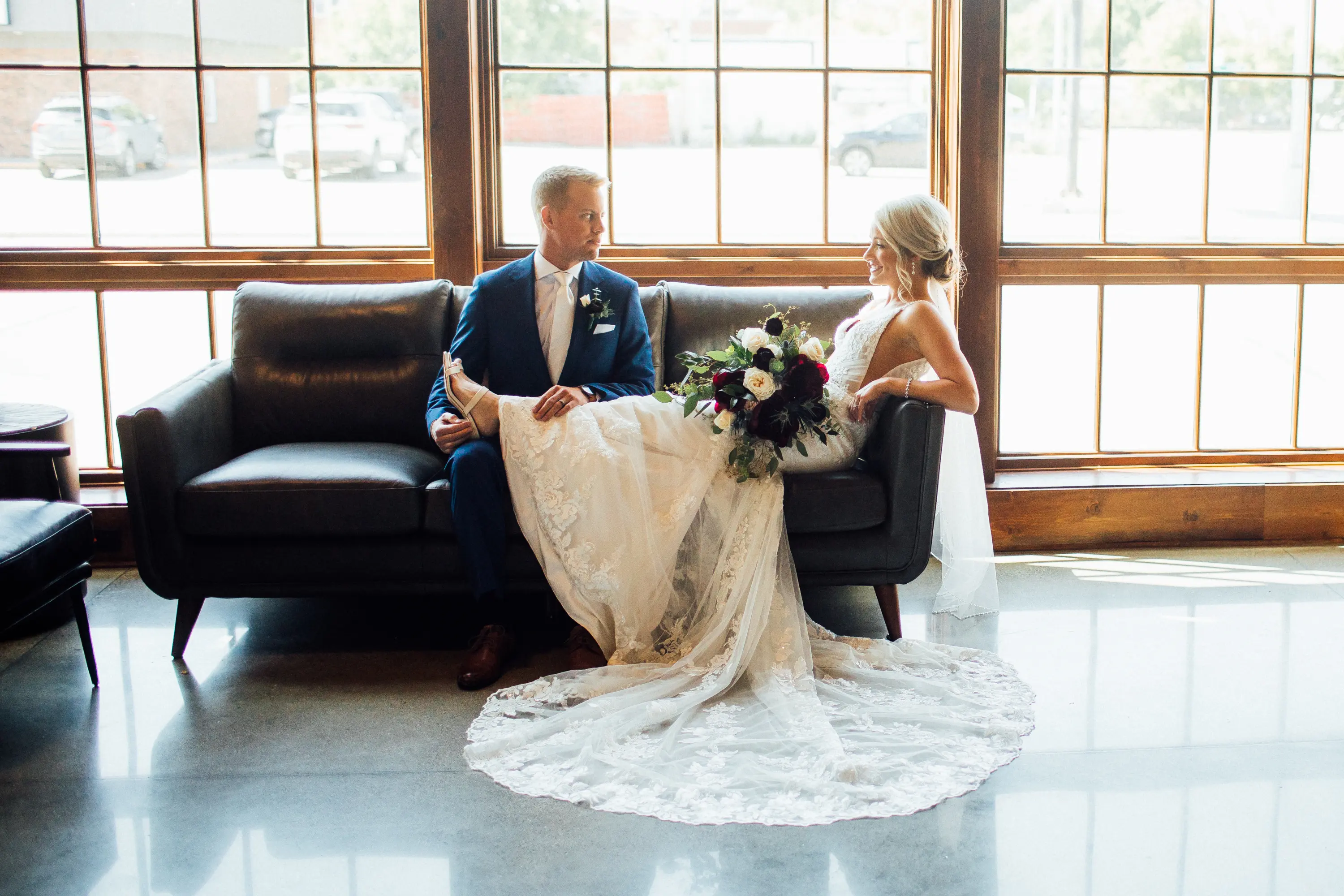 Bride Wearing Graceful Sparkly Lace Wedding Dress Called Fontaine By Maggie Sottero Sitting With Groom On A Couch