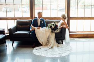 Bride Wearing Graceful Sparkly Lace Wedding Dress Called Fontaine By Maggie Sottero Sitting With Groom On A Couch