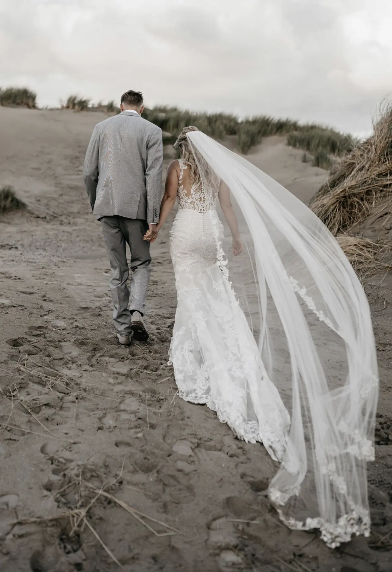 Bride Wearing Lace Fit-And-Flare Wedding Dress Called Hamilton By Sottero And Midgley And Groom Walking On The Beach