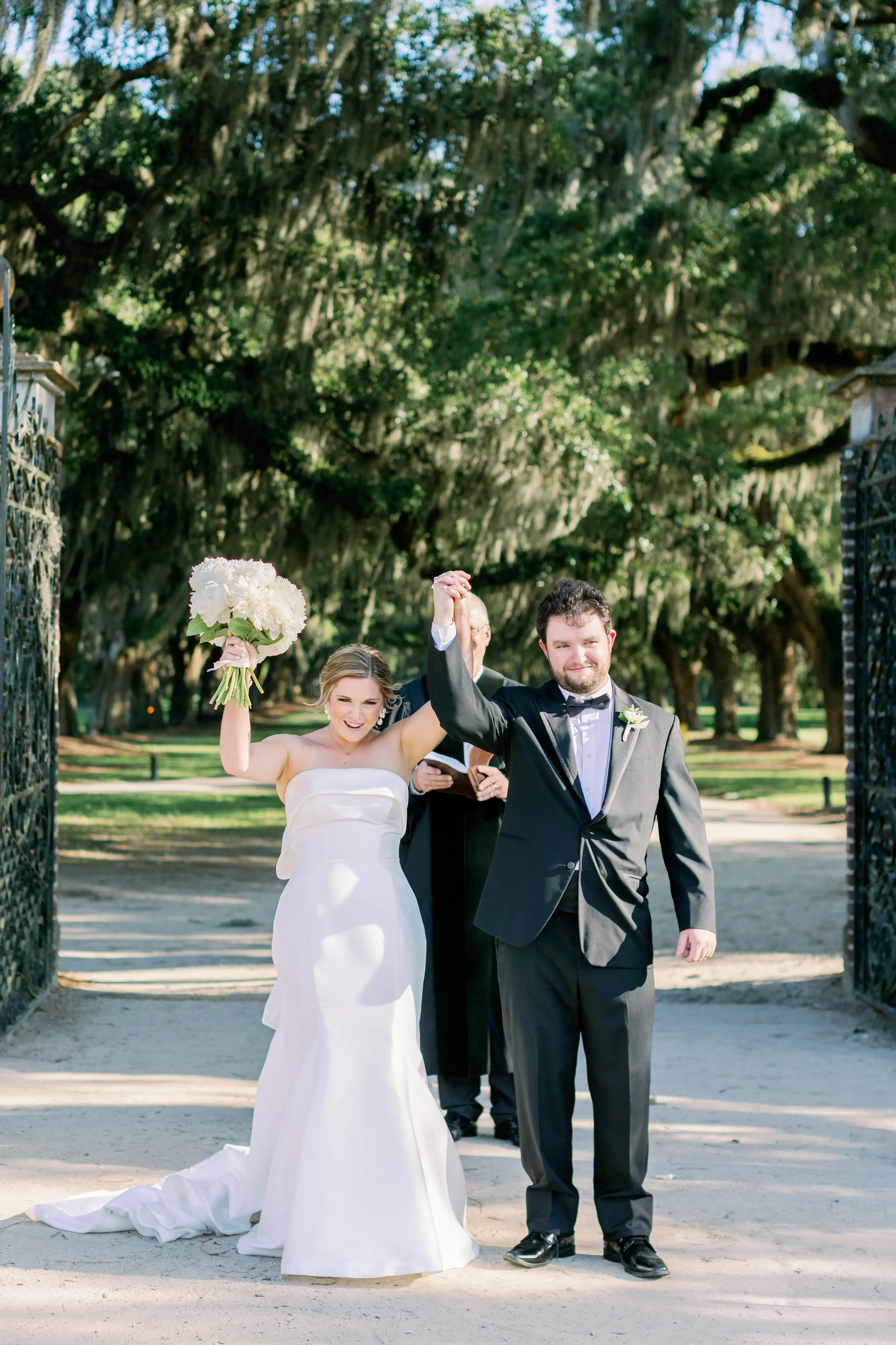Bride with groom wearing strapless elegant mermaid wedding dress outdoors holding flower bouquet.