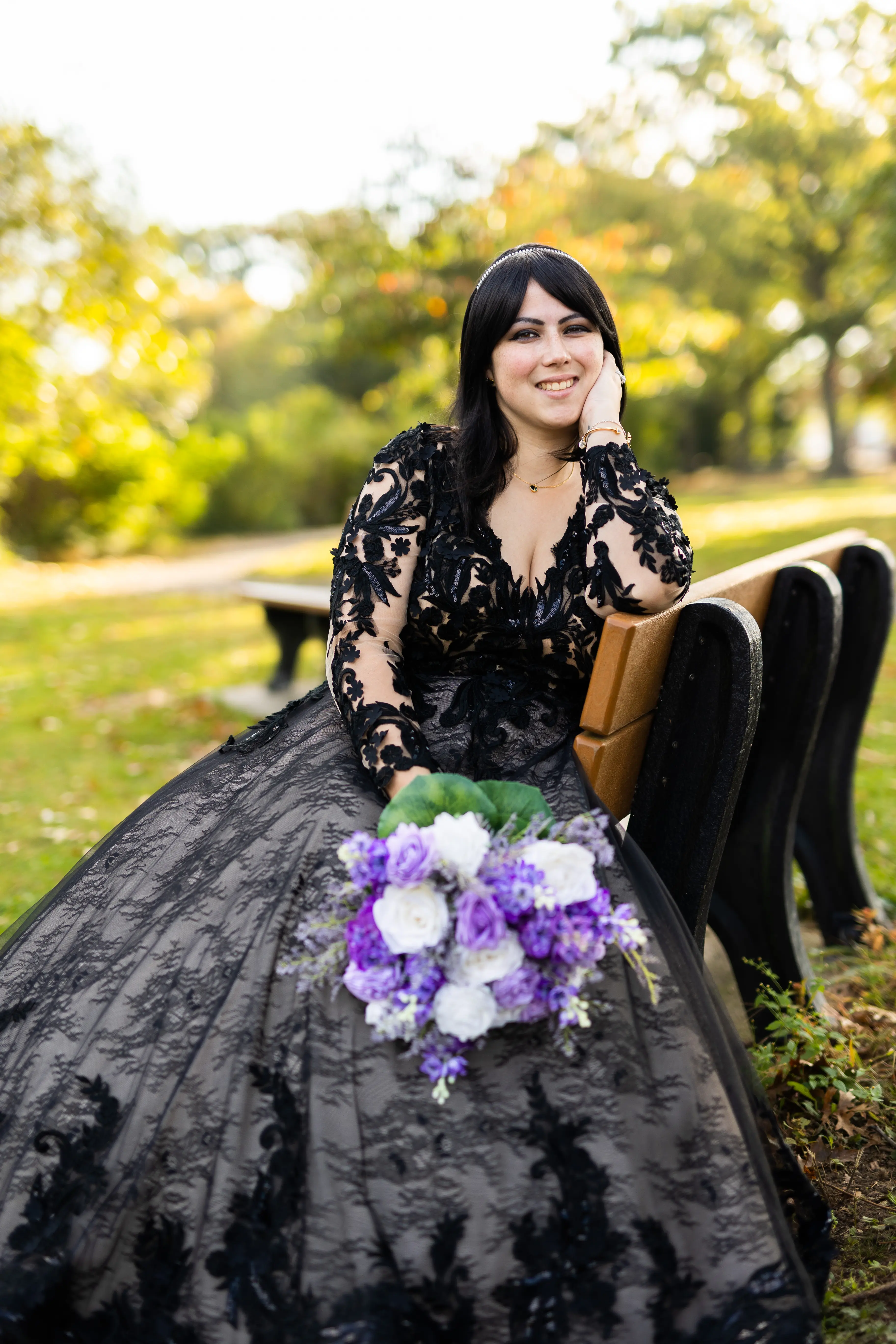 Bride Sitting Down Wearing Long Sleeve Black Lace Ballgown Wedding Dress Holding Bridal Bouquet.