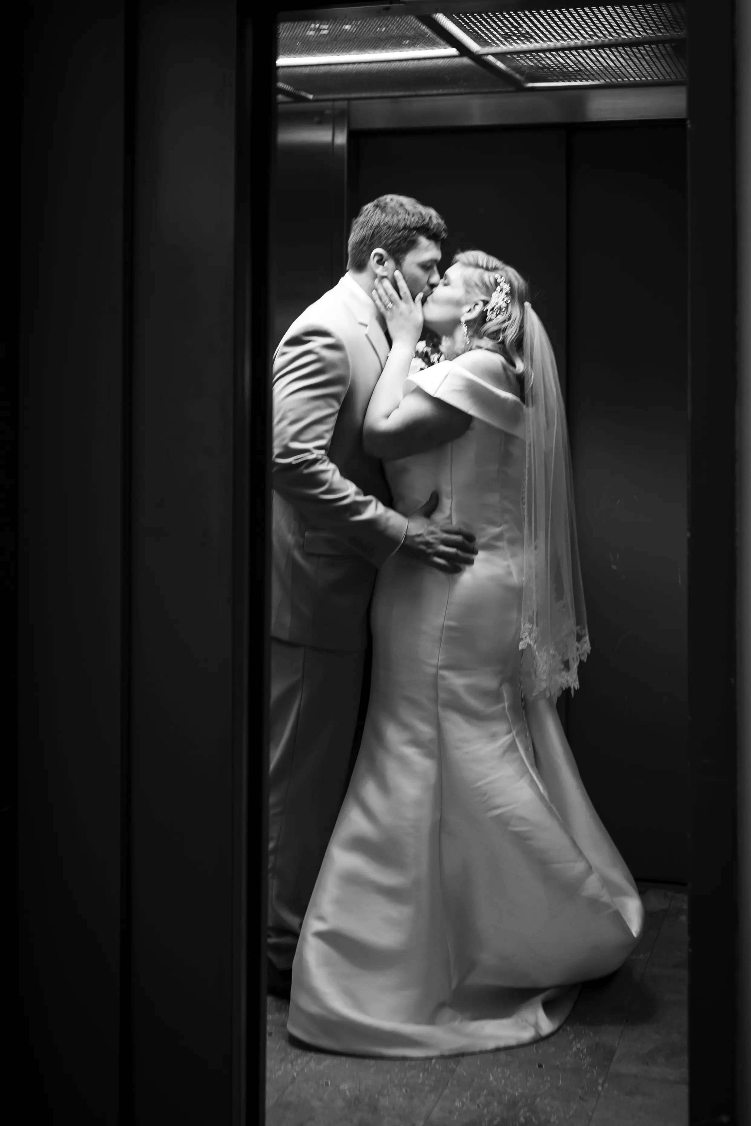 Bride And Groom Share Kiss. Bride Wearing Vintage Glamour Timeless Off-The-Shoulder Fit-And-Flare Wedding Dress Called Josie By Rebecca Ingram