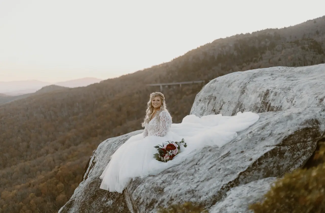 Bride Sitting On Mountain Rock In Lacey Long Sleeve Ball Gown Wedding Dress Named Mallory Dawn By Maggie Sottero
