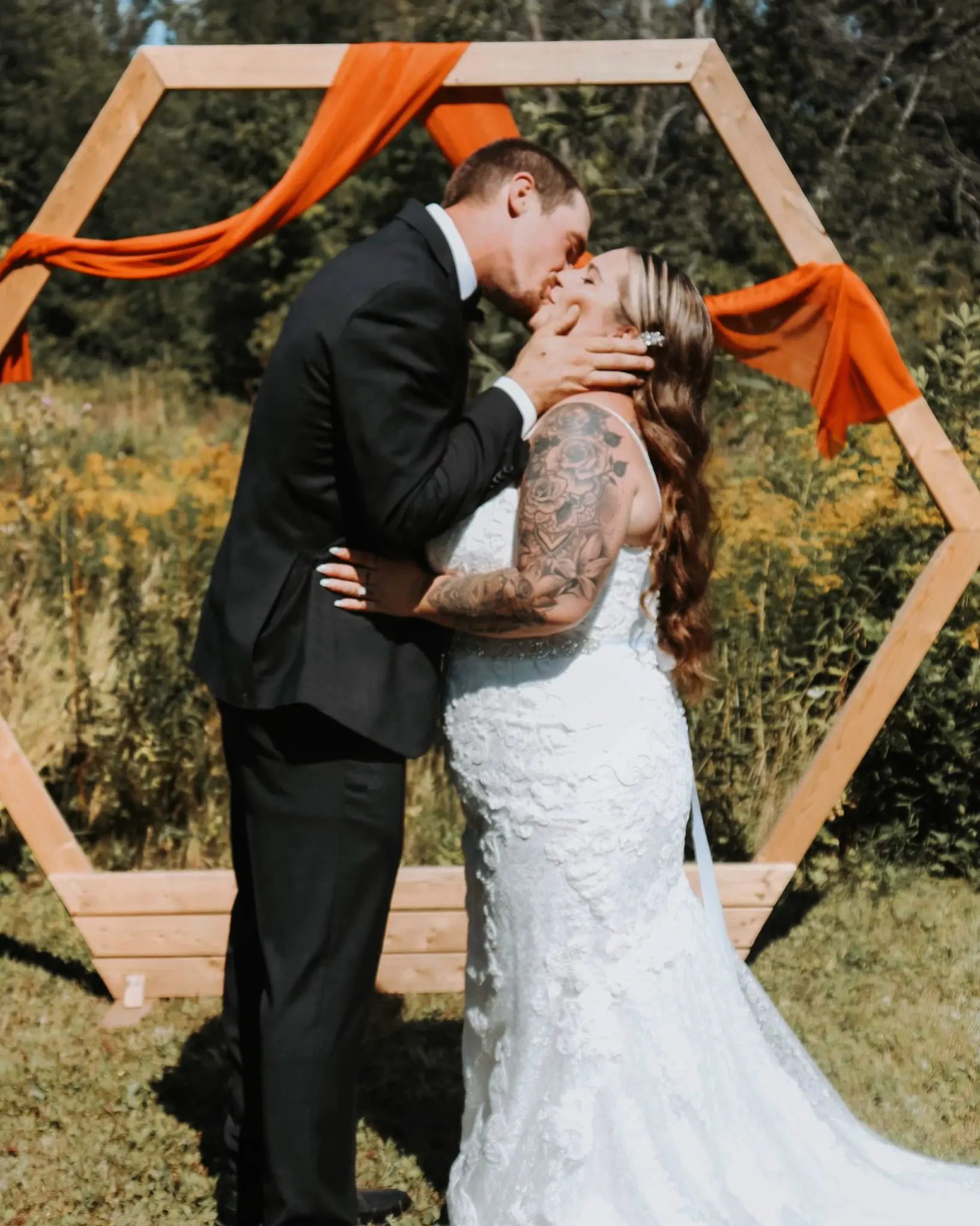 Bride Wearing Sheath Lace Wedding Dress With Beaded Belt Called Tuscany Lynette By Maggie Sottero Kisses Groom By Hexagon Structure