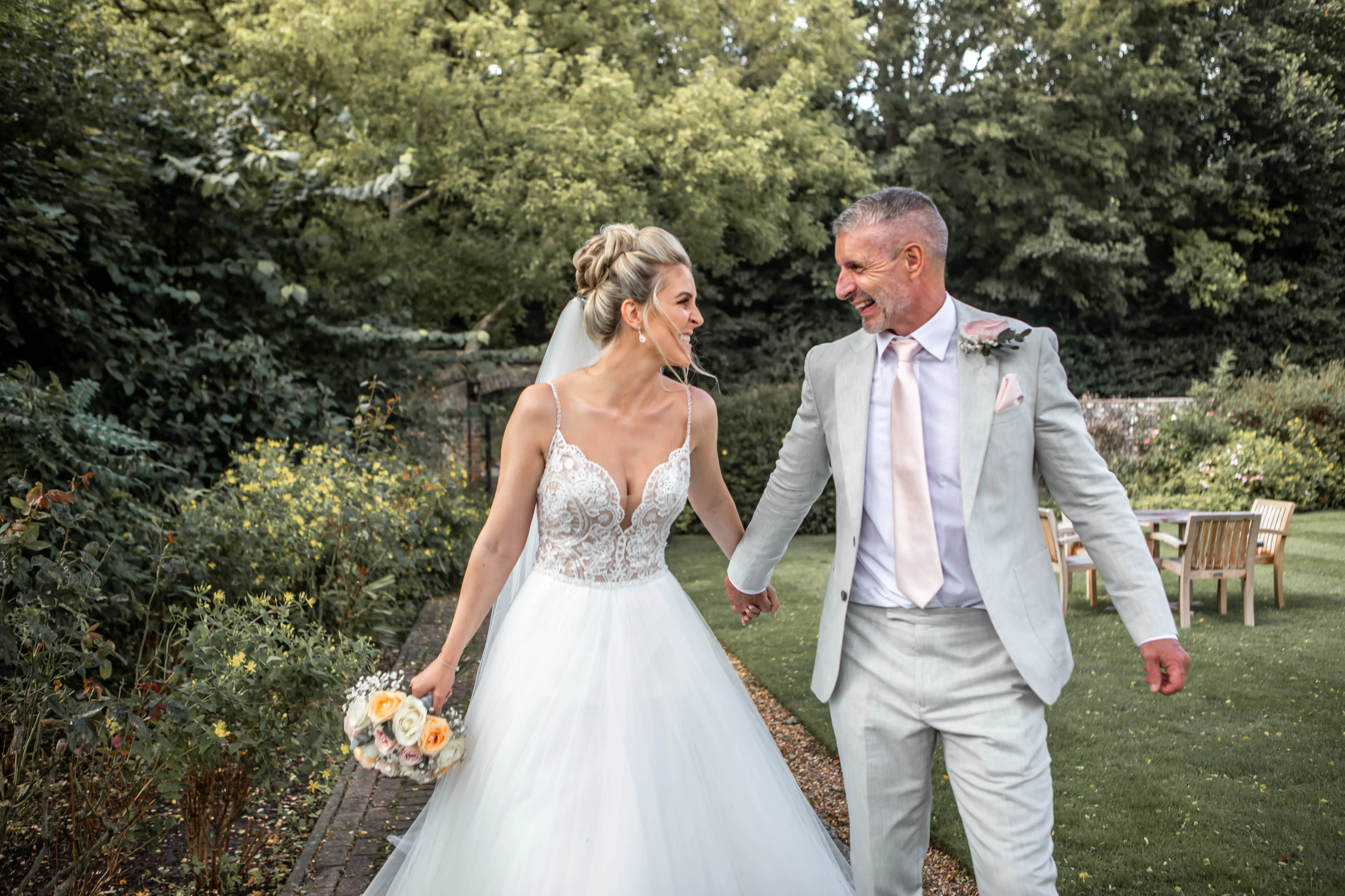 Bride and groom hand in hand, laughing and looking at each other.