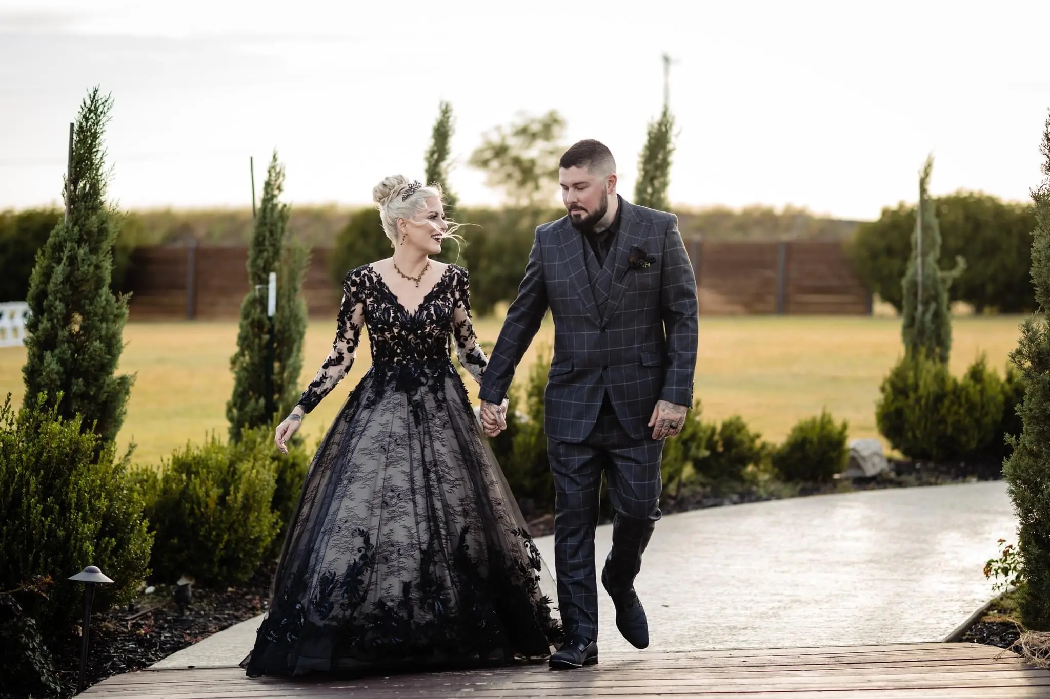 Bride Wearing Black Lace Wedding Dress Called Zander By Sottero And Midgley Holding Hands With Groom Walking On A Path