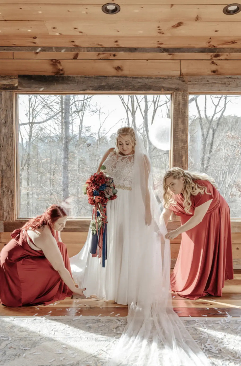 Bride In Chiffon Wedding Dress Called Tasha By Rebecca Ingram With Red And Blue Rose Bouquet And Bridesmaids In Red