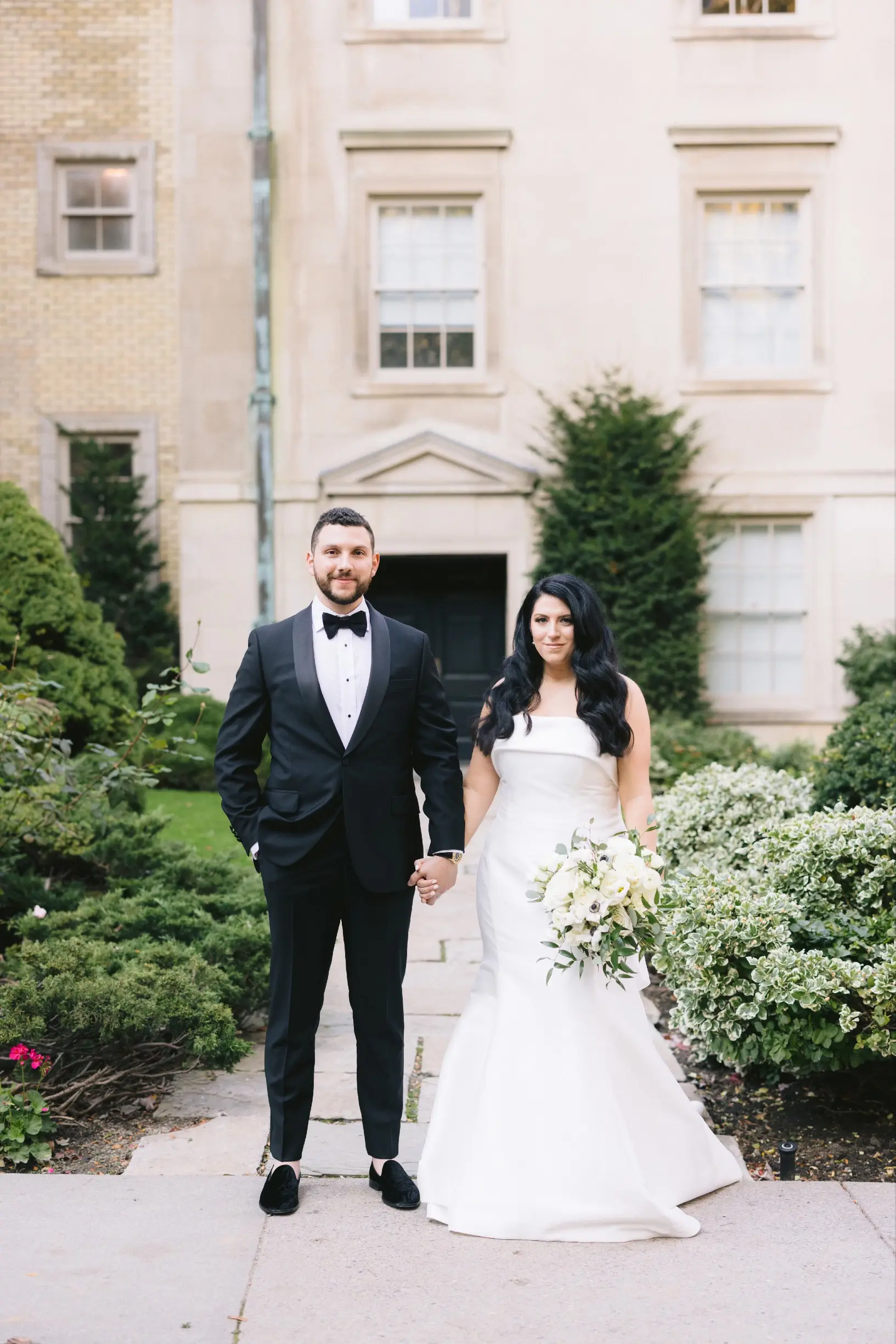 Bride with groom wearing strapless satin mermaid wedding dress with big bow on the back.