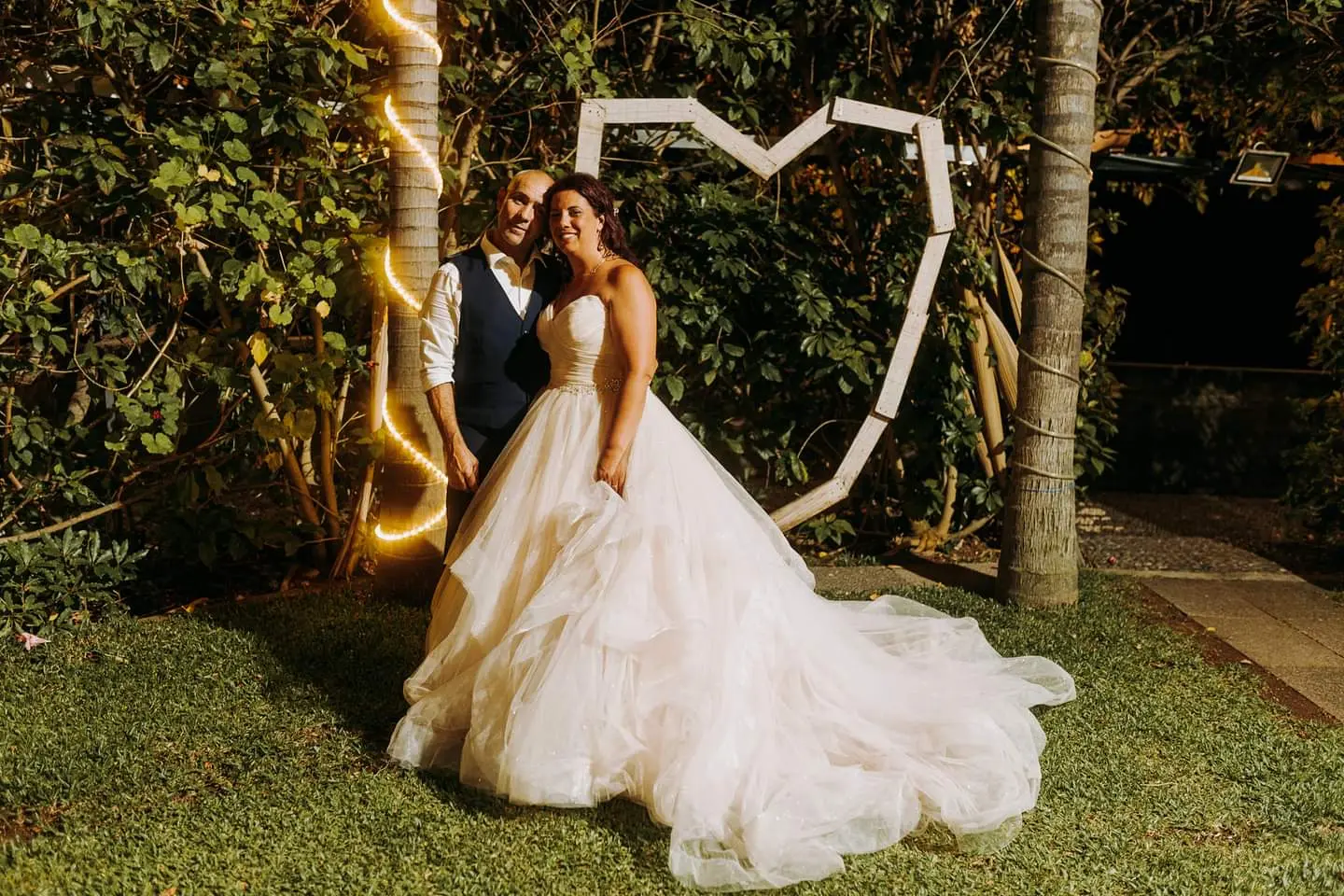 Bride Wearing Sparkly Ballgown Wedding Dress Called Yasmin By Maggie Sottero With Groom Near A Heart Shaped Sculpture