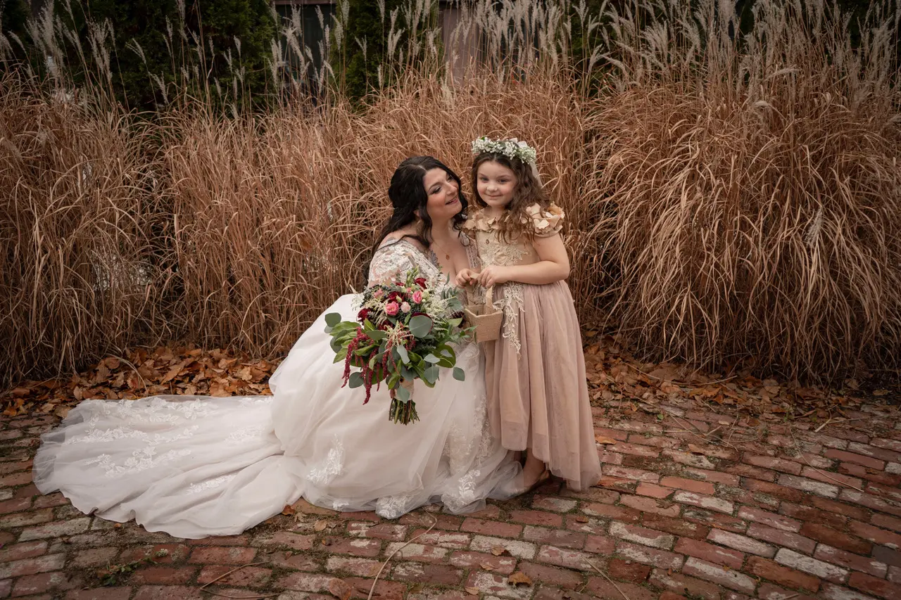 Bride holding mixed flower bouquet knelt down next to flowergirl.
