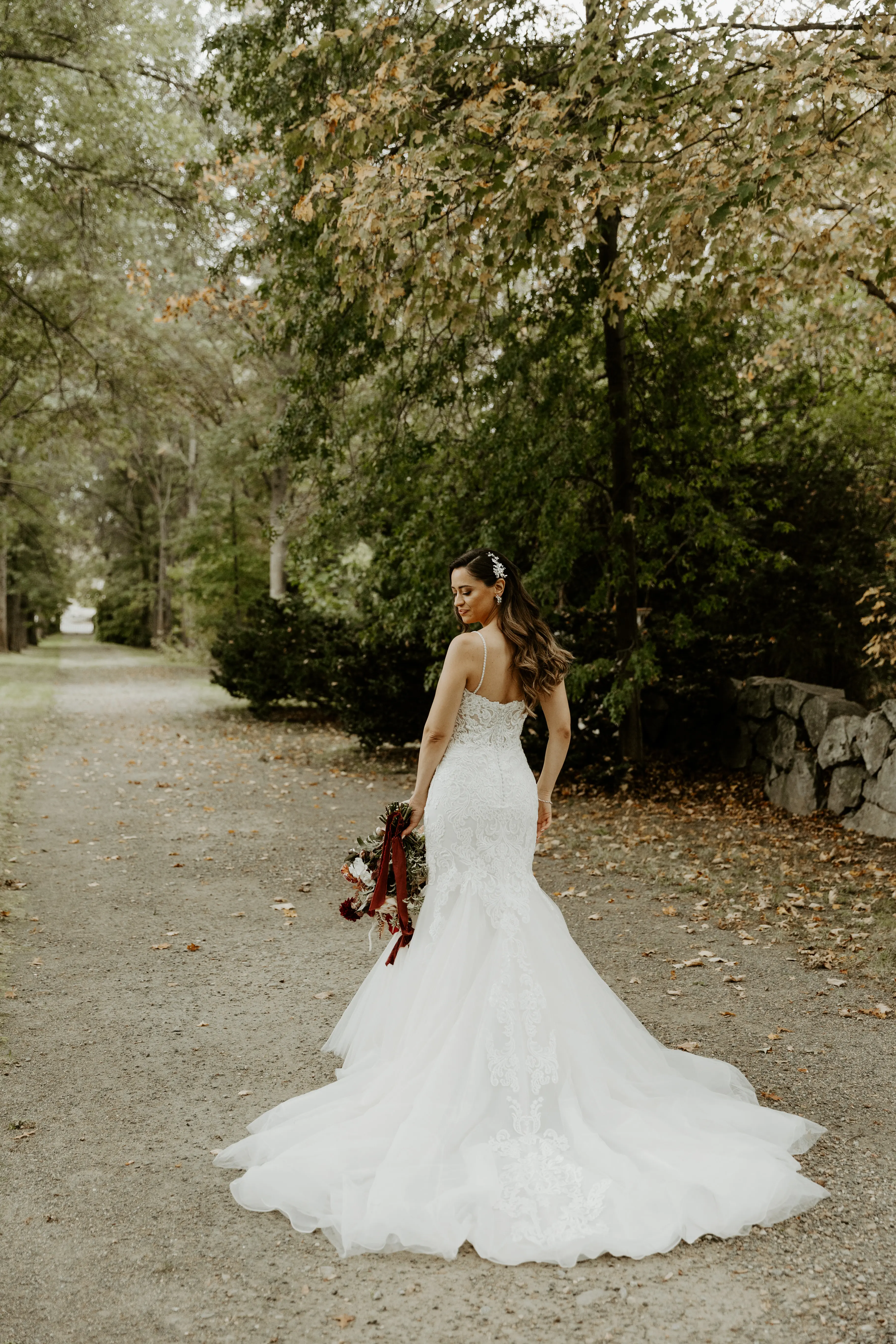 Bride wearing lace fit-and-flare wedding dress holding bridal bouquet outdoors.