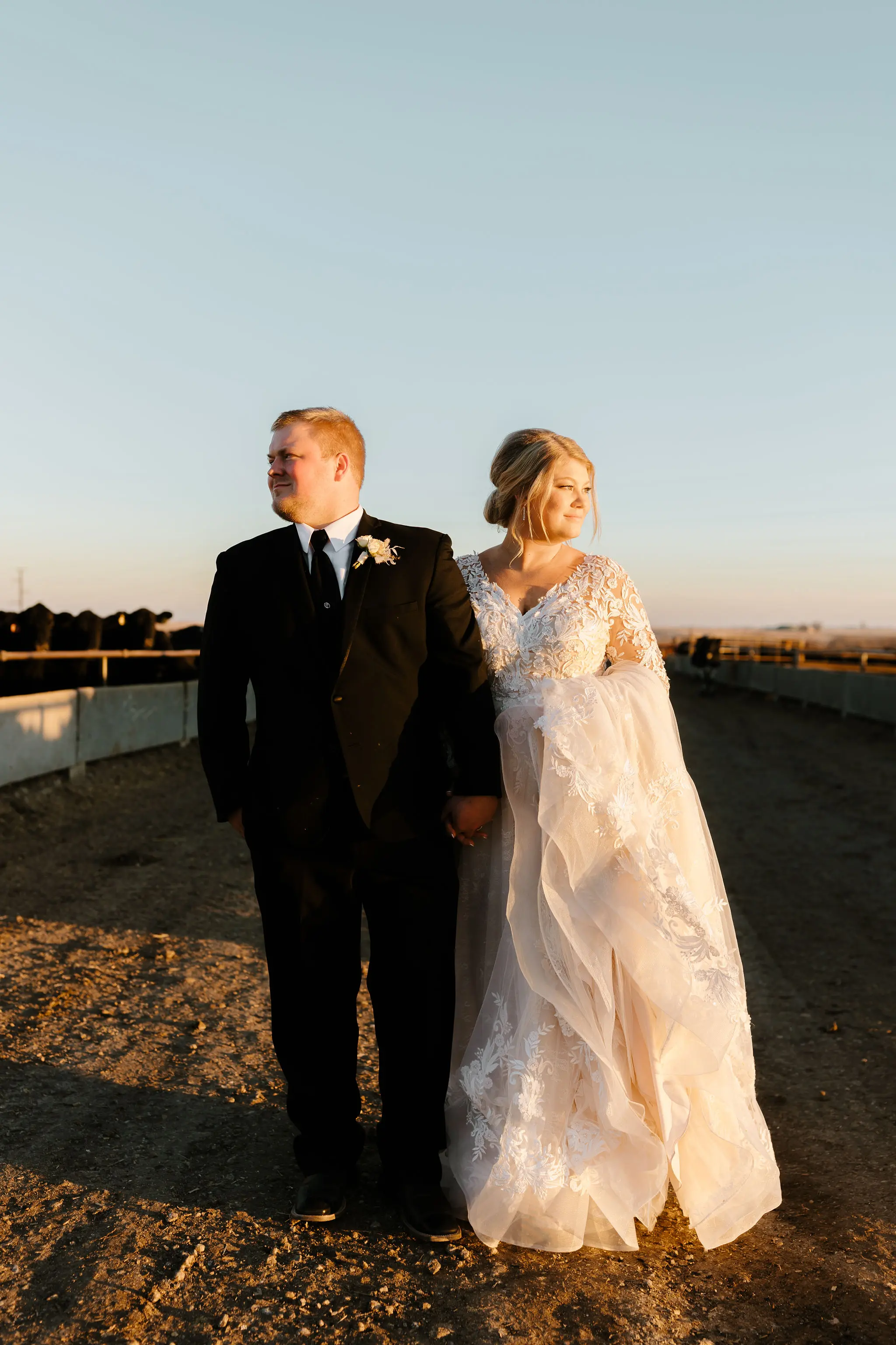 Bride And Groom Standing Together. Bride Wearing Layered Ball Gown Wedding Dress With Long Sleeves Called Zander By Sottero And Midgley