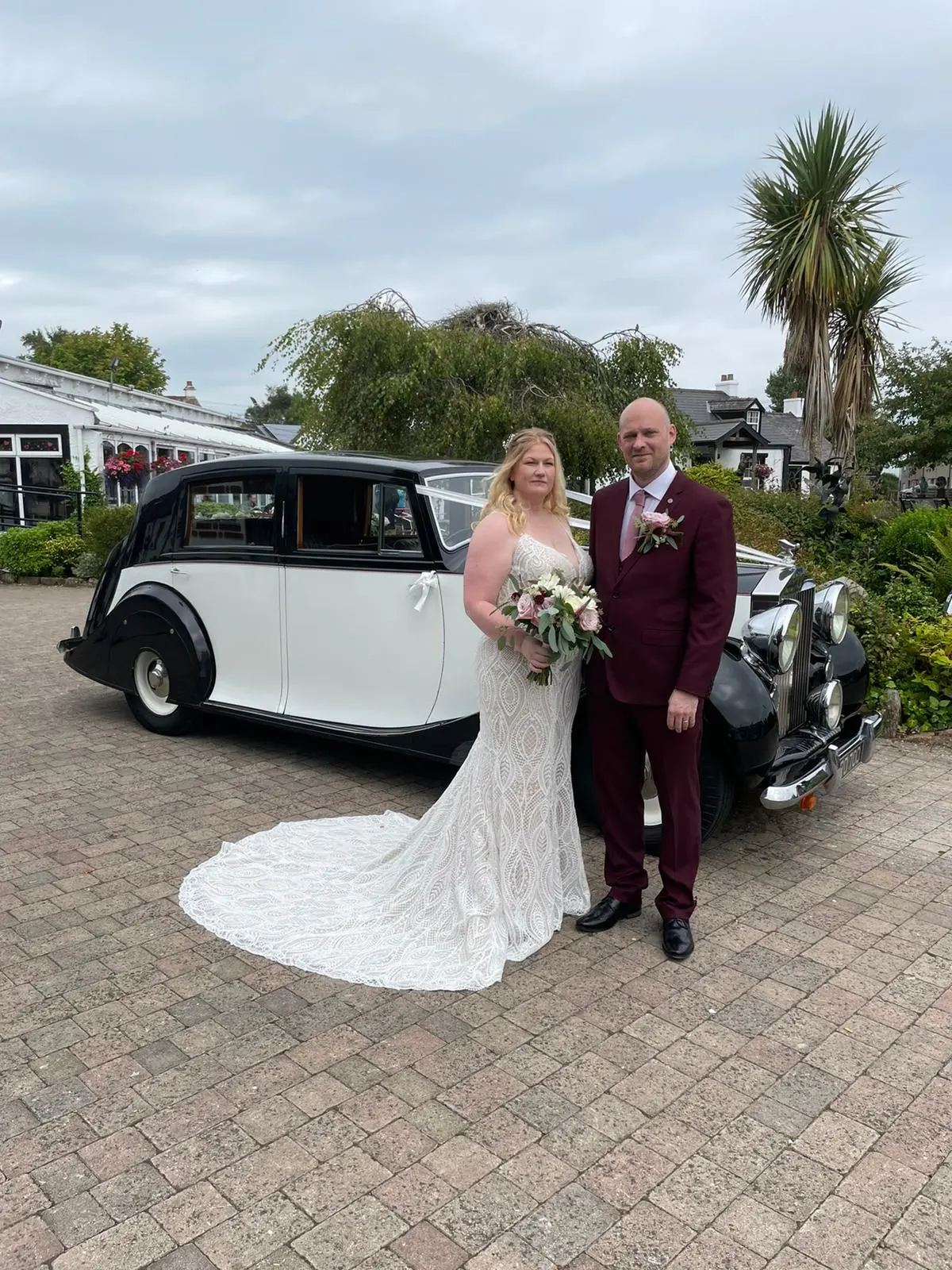 Bride wearing wedding dress called Daxton stood with groom in front of vintage car.