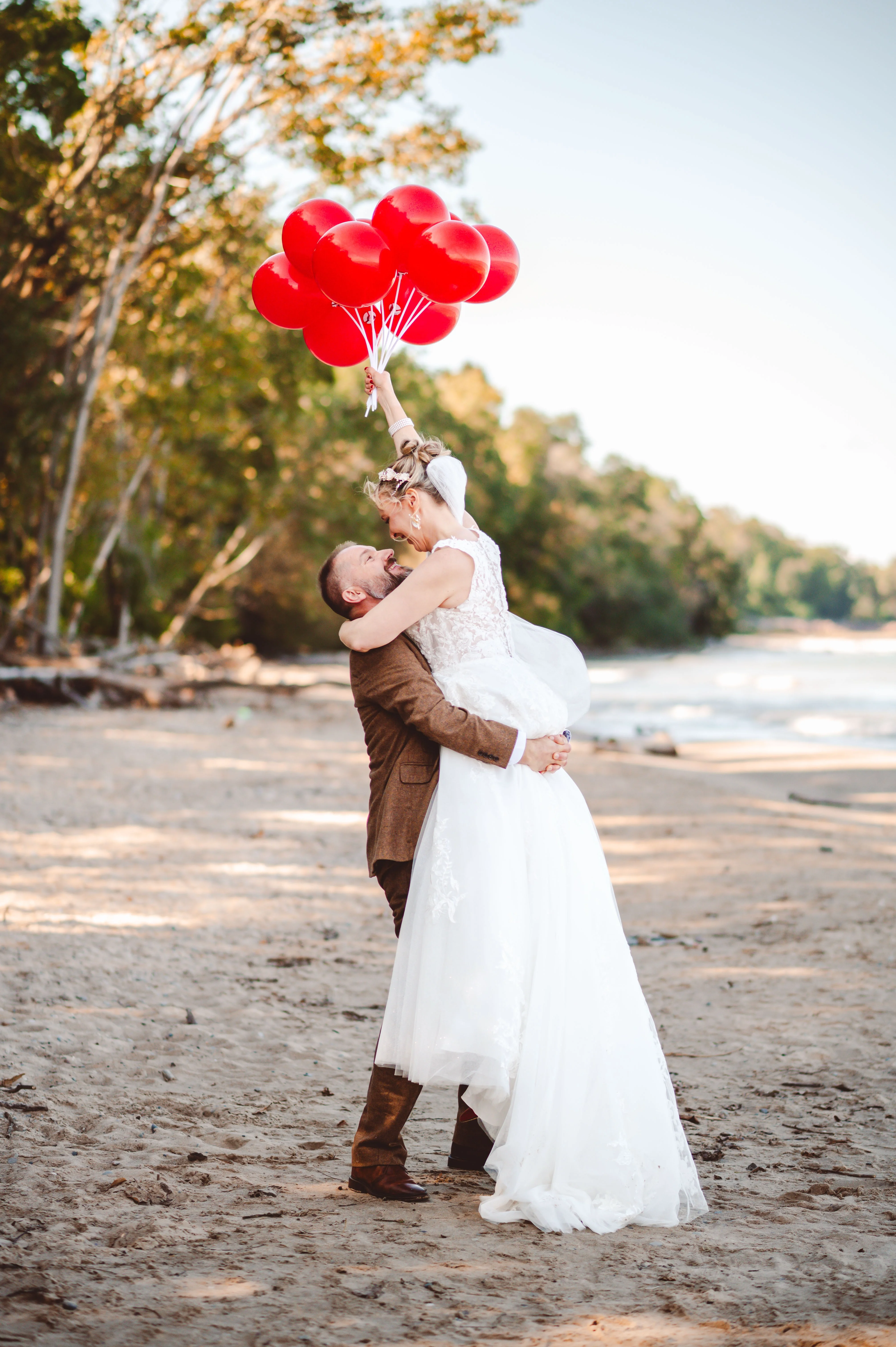 Bride wearing Lace Aline Wedding Dress Called Rickie By Rebecca Ingram With Groom Lifting Her Up With Red Balloons