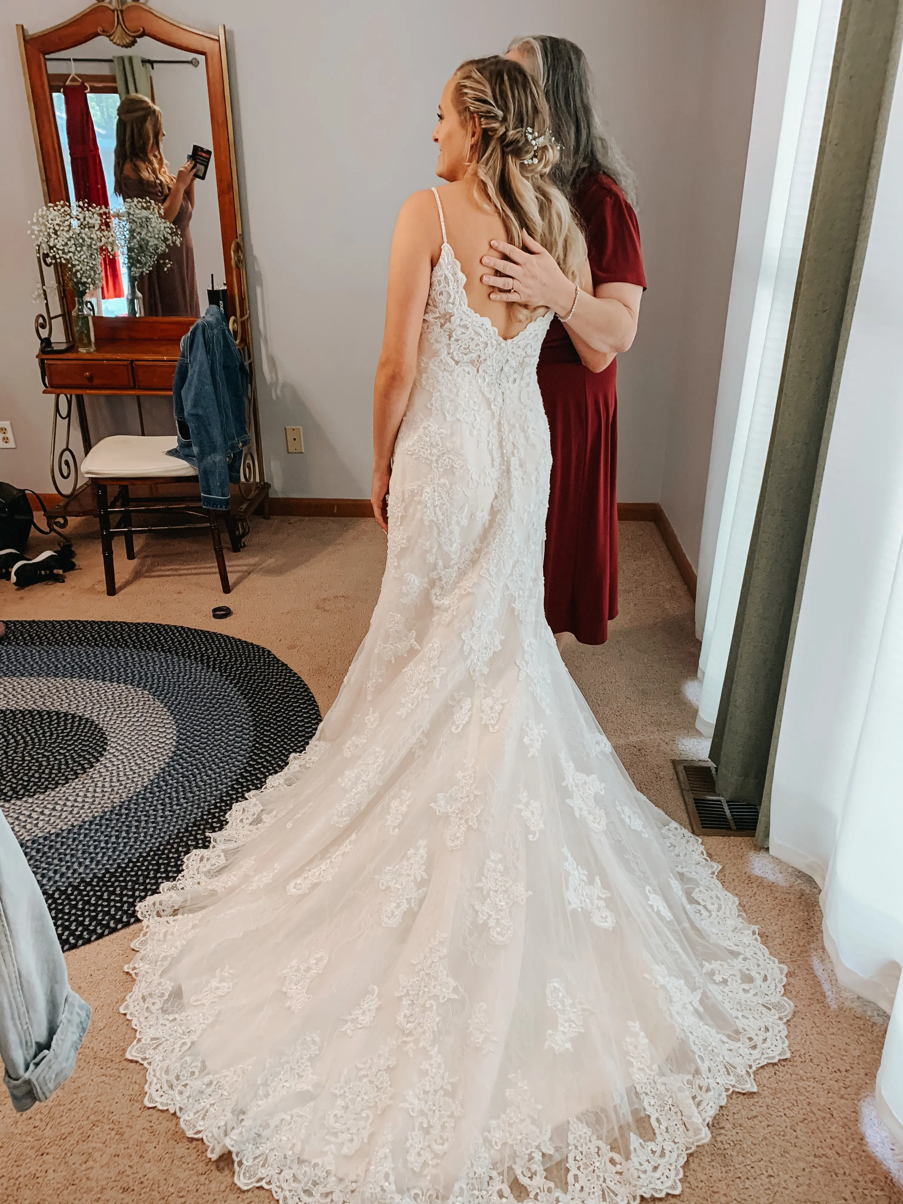 Bride posing with mother while bridesmaid takes a photo.