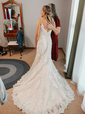 Bride posing with mother while bridesmaid takes a photo.