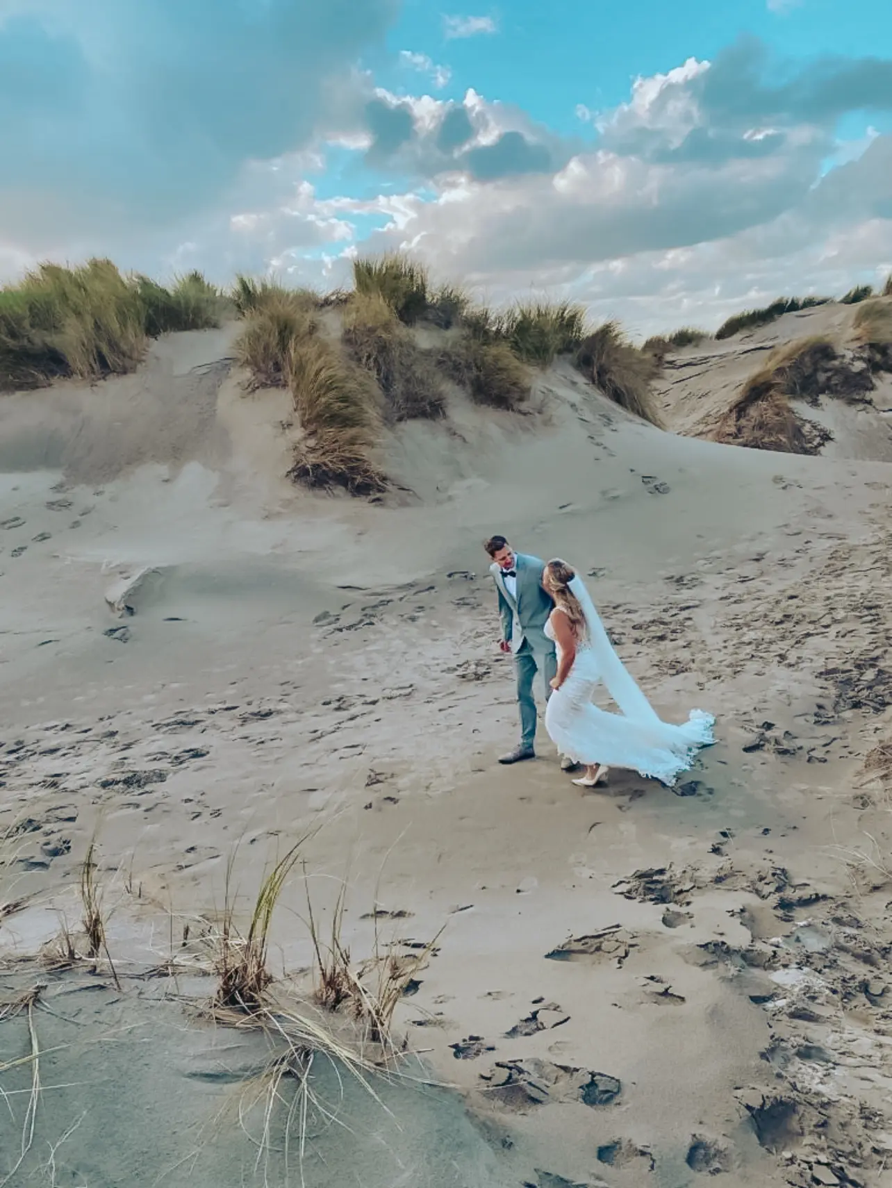 Bride Wearing Lace Fit-And-Flare Wedding Dress Called Hamilton By Sottero And Midgley Walking On The Sand With Groom