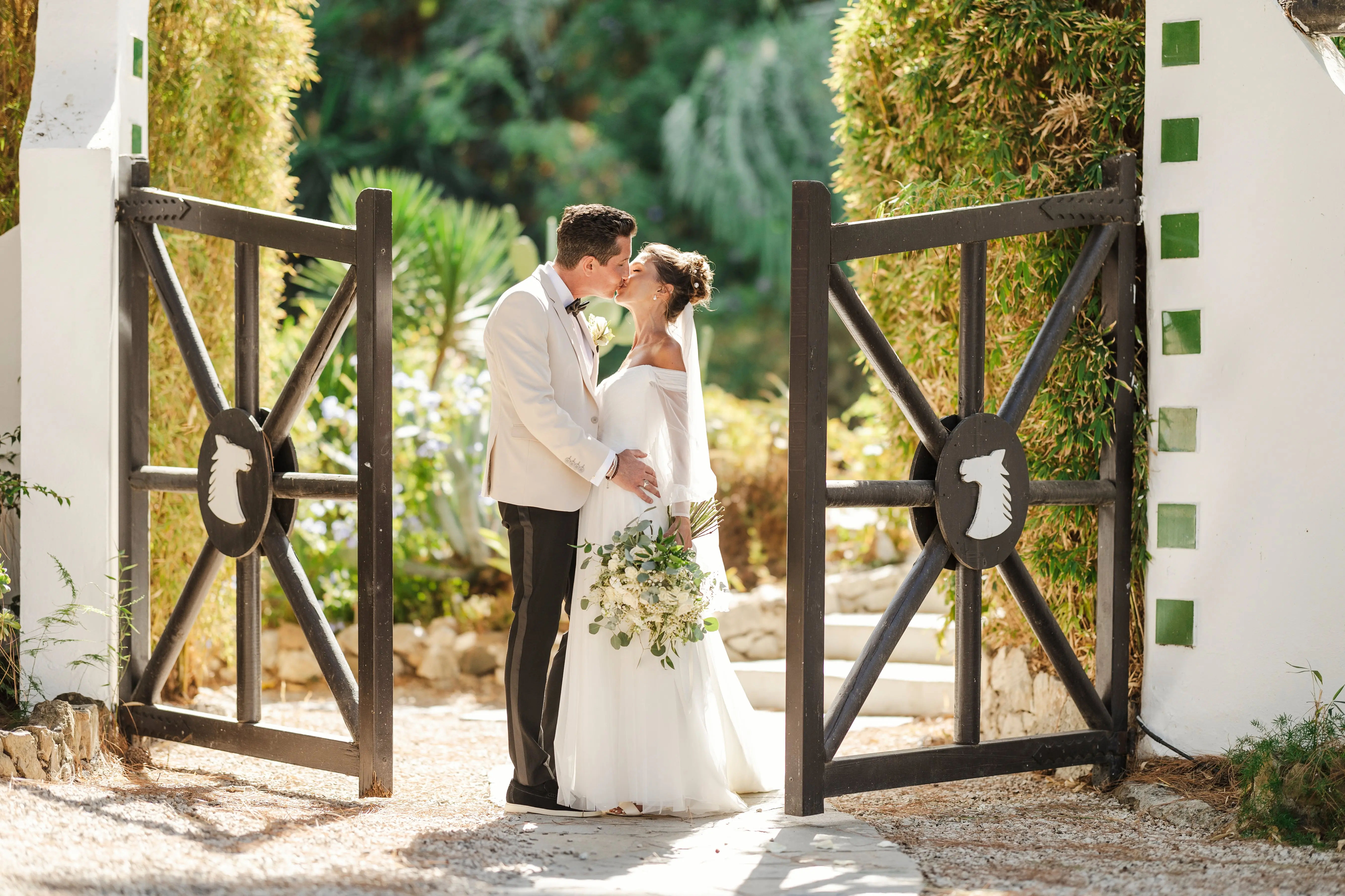 Bride Wearing Aline Wedding Dress Called Nerida By Sottero And Midgley Kissing Groom Next To A Gate