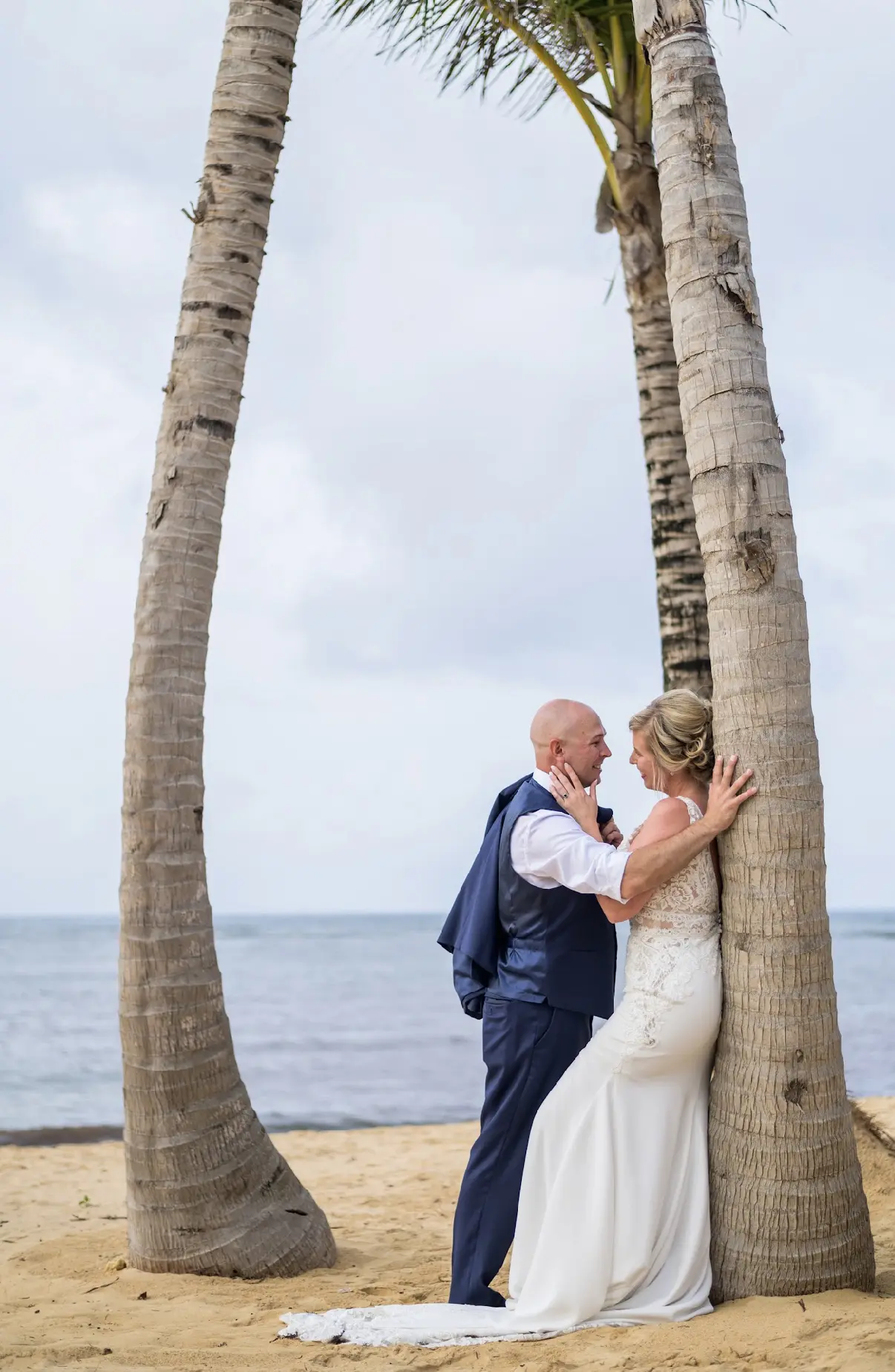 Bride leaning against tree with groom moving in for a kiss.