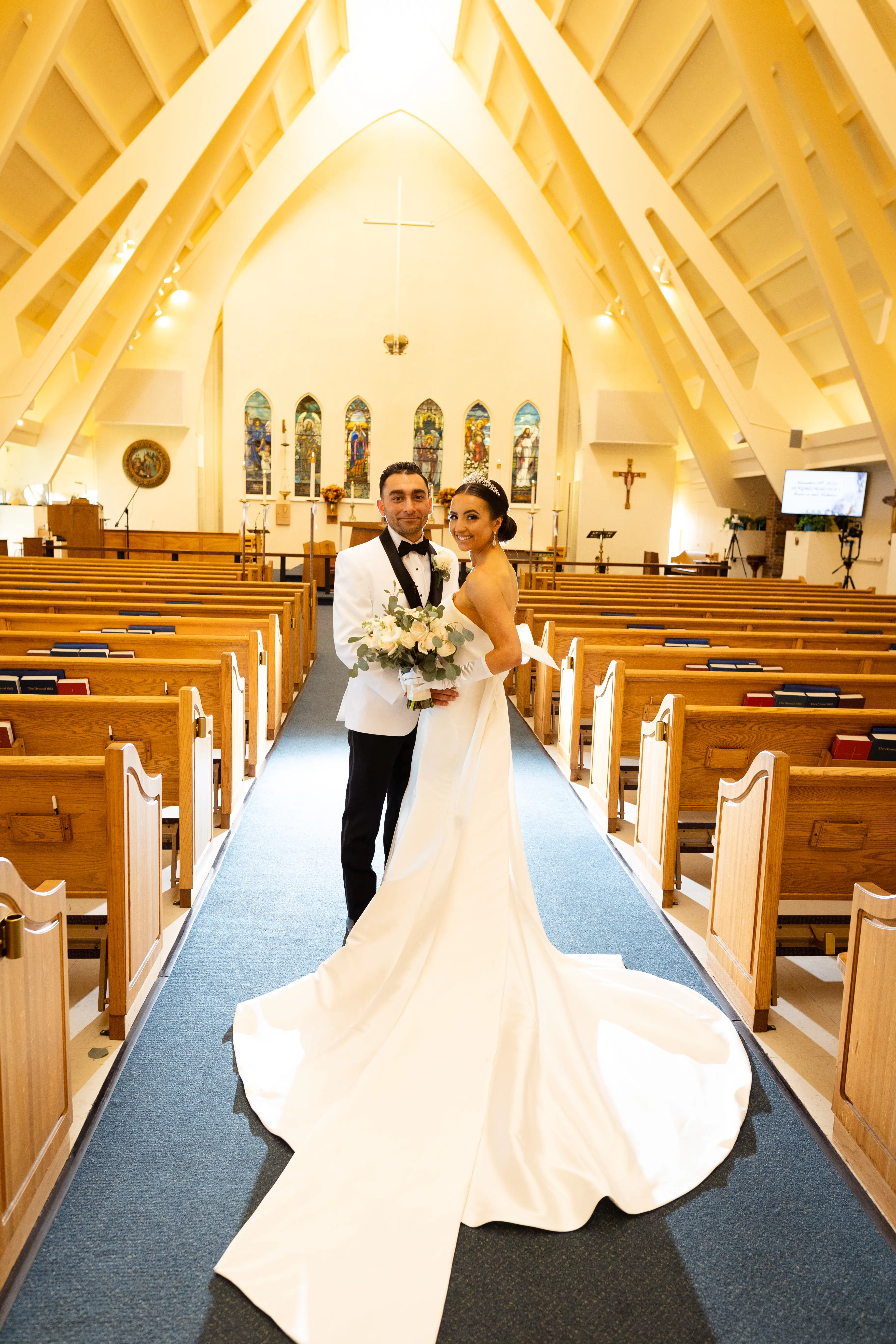 Bride And Groom Standing In Chapel. Bride Wearing Unique Strapless Wedding Gown With Statement Bow Called Mitchell By Maggie Sottero