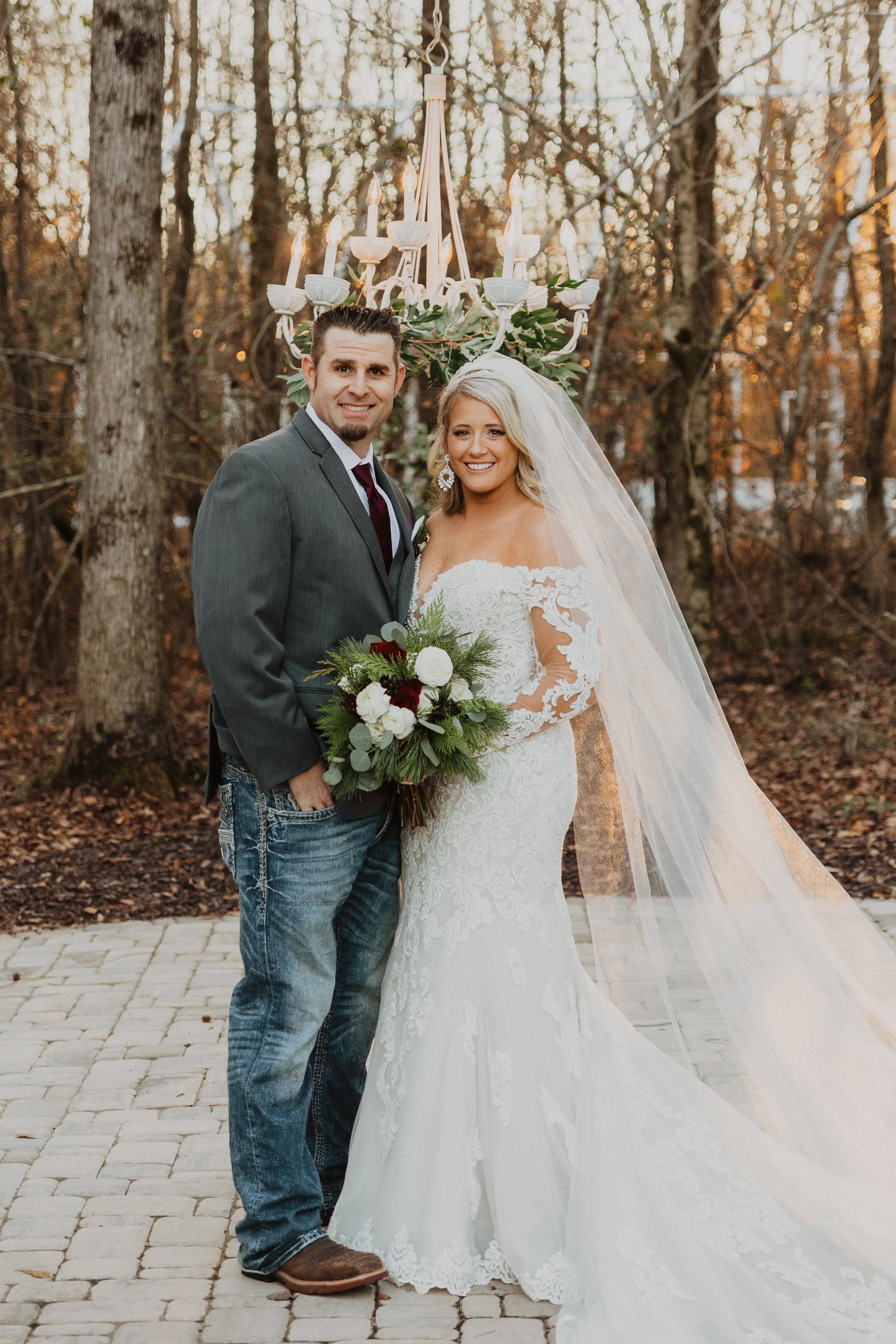 Groom Smiling With Bride In A White Wedding Dress With Off-The-Shoulder Sleeves Named Fiona By Maggie Sottero With A Long Veil And Flower Bouquet
