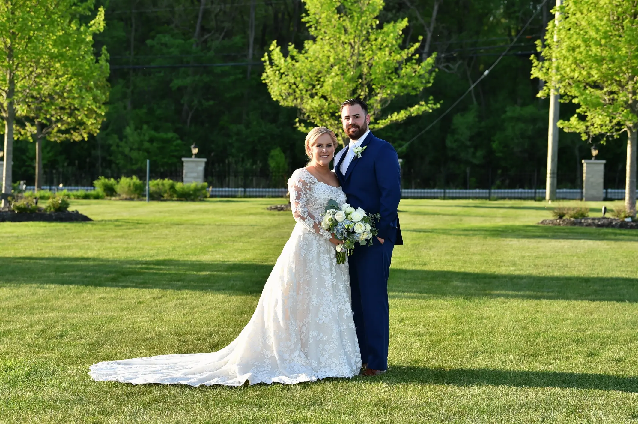 Bride Wearing Long Sleeve Floral Lace Wedding Dress Called Sawyer By Sottero and Midgley Posing With Groom On Green Grass