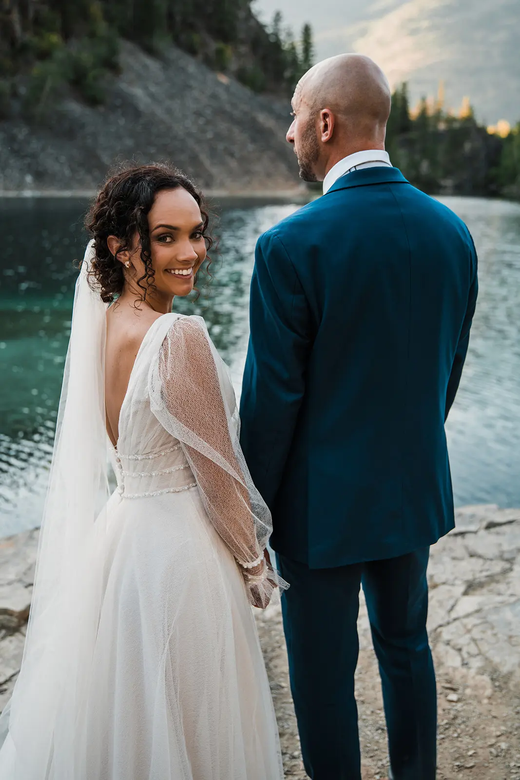 Groom with Bride by Lake Wearing Wedding Dress Called Joanne by Rebecca Ingram.