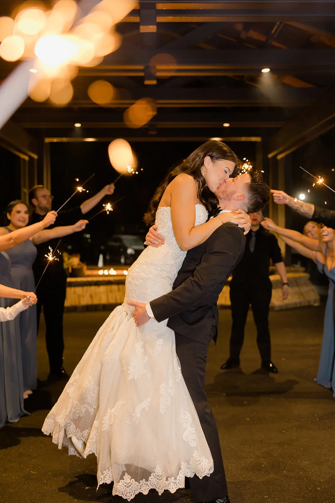 Bride And Groom Exit Kiss With Sparklers. Bride Wearing Lace Wedding Gown Called Fiona By Maggie Sottero