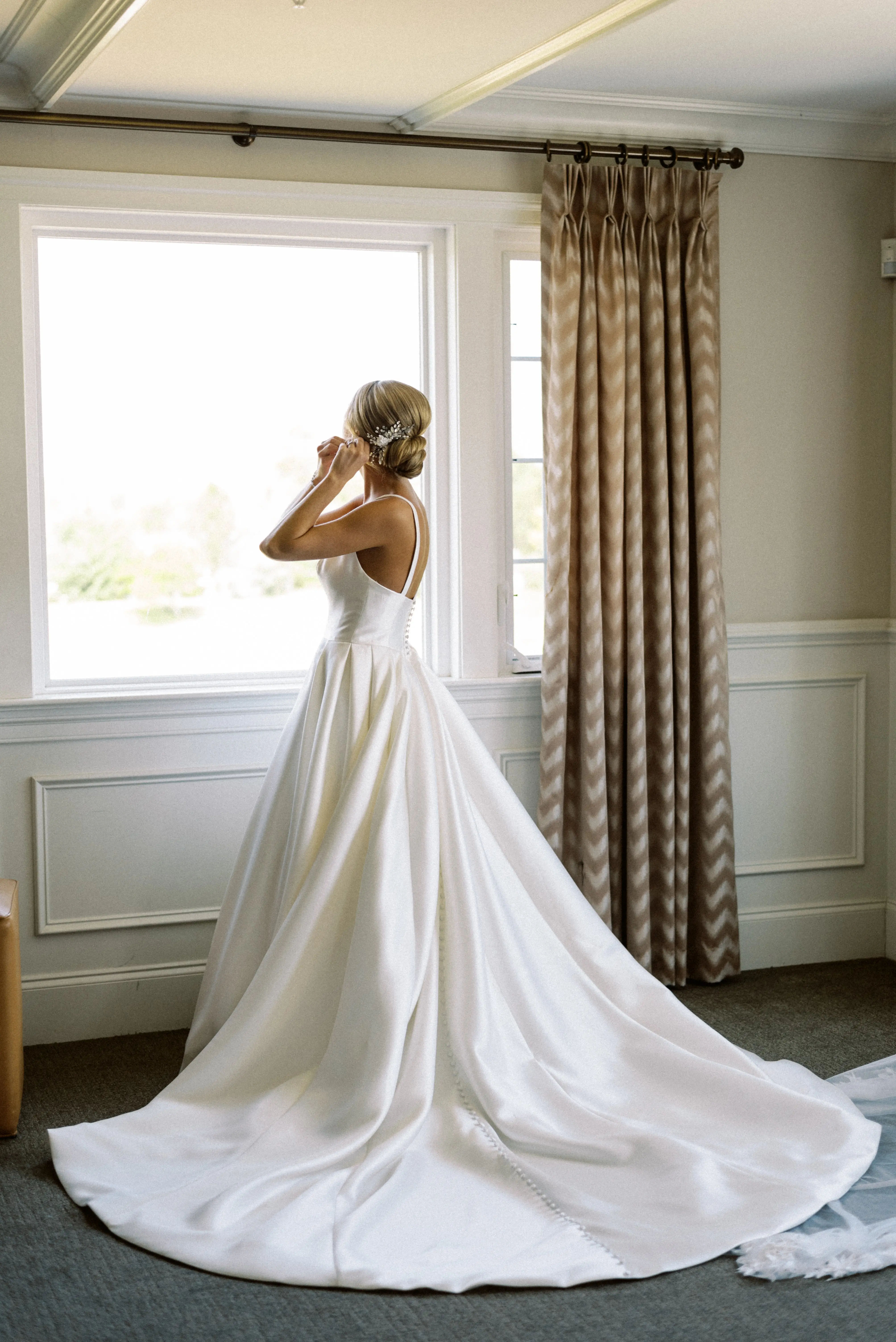 Bride wearing Selena wedding dress by Maggie Sottero putting on earrings