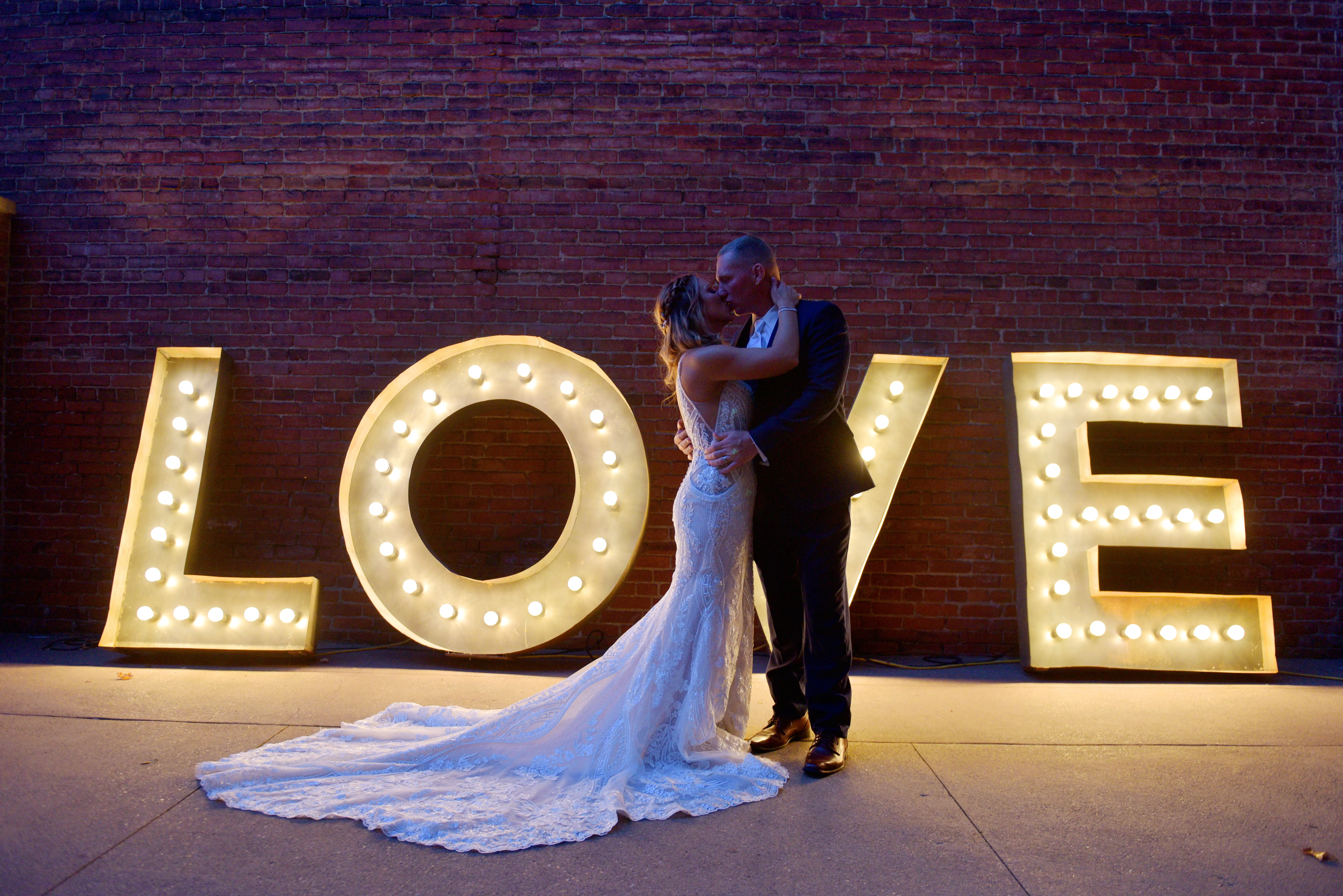 Groom Kissing Bride in V-Neckline Wedding Gown Accented with Beaded Detail Called Bailey by Sottero & Midgley