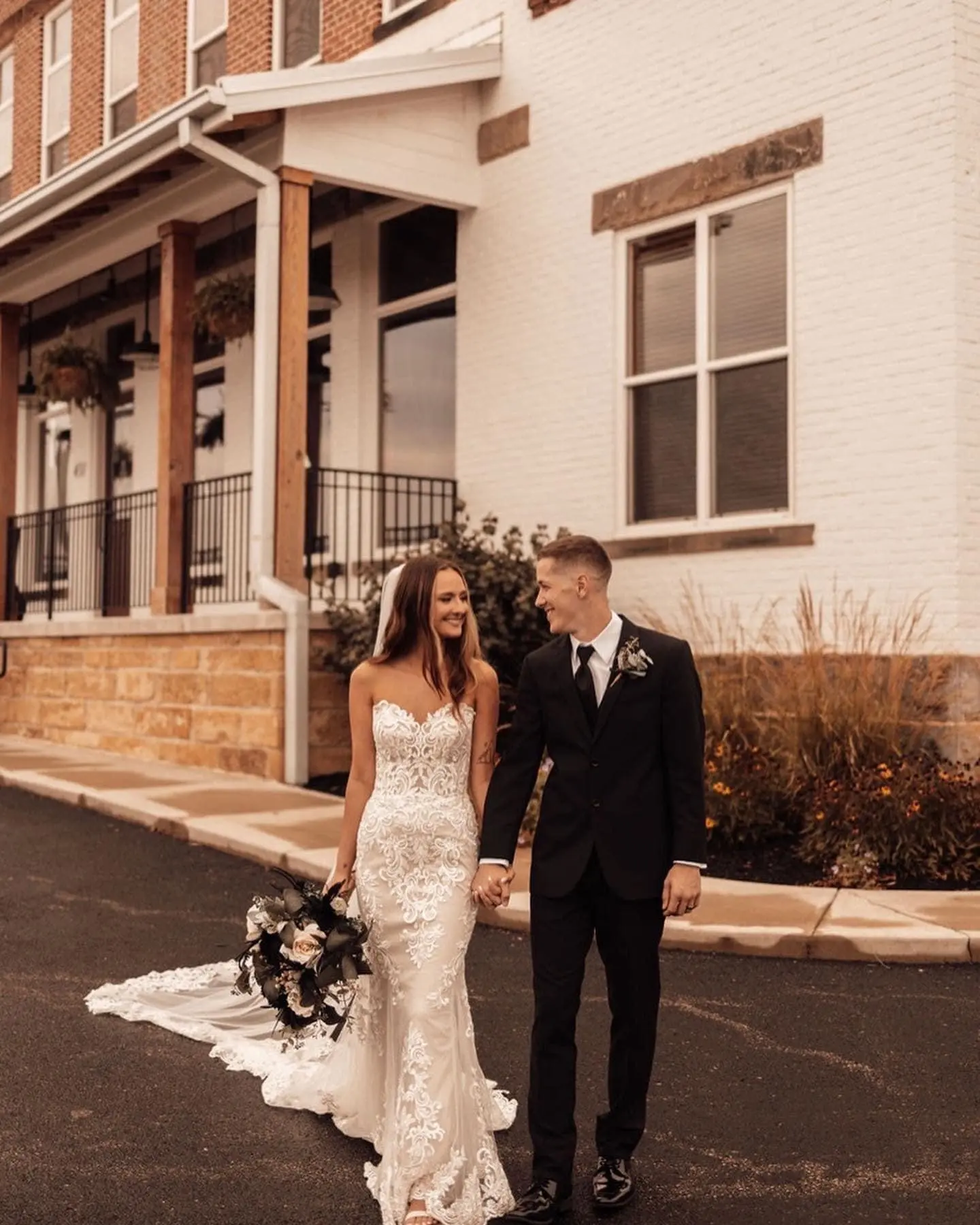Bride with groom outdoors wearing strapless lace fit and flare wedding dress.