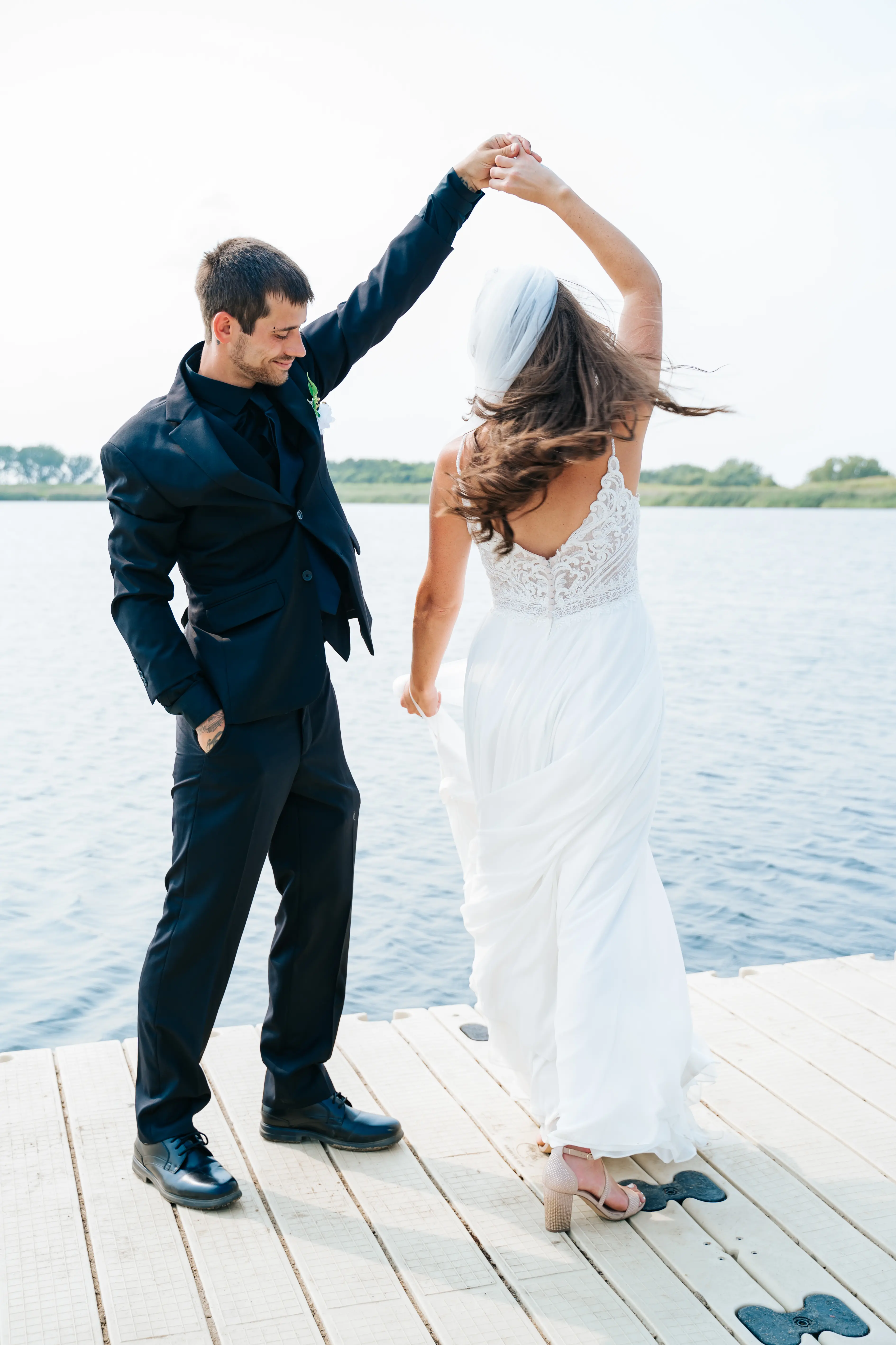 Bride Wearing Beach Sheath Wedding Dress Called Lorraine By Rebecca Ingram Dancing On A Dock With Groom