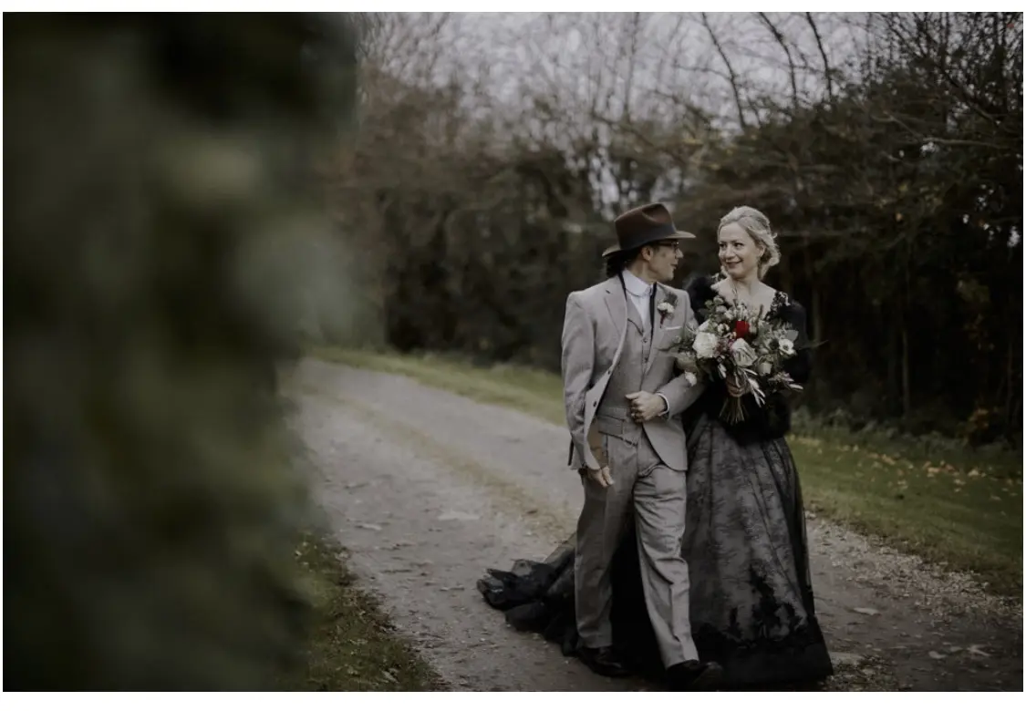 Bride Wearing Black Lace Wedding Gown Called Zander By Sottero and Midgley With Groom Walking Through a Garden