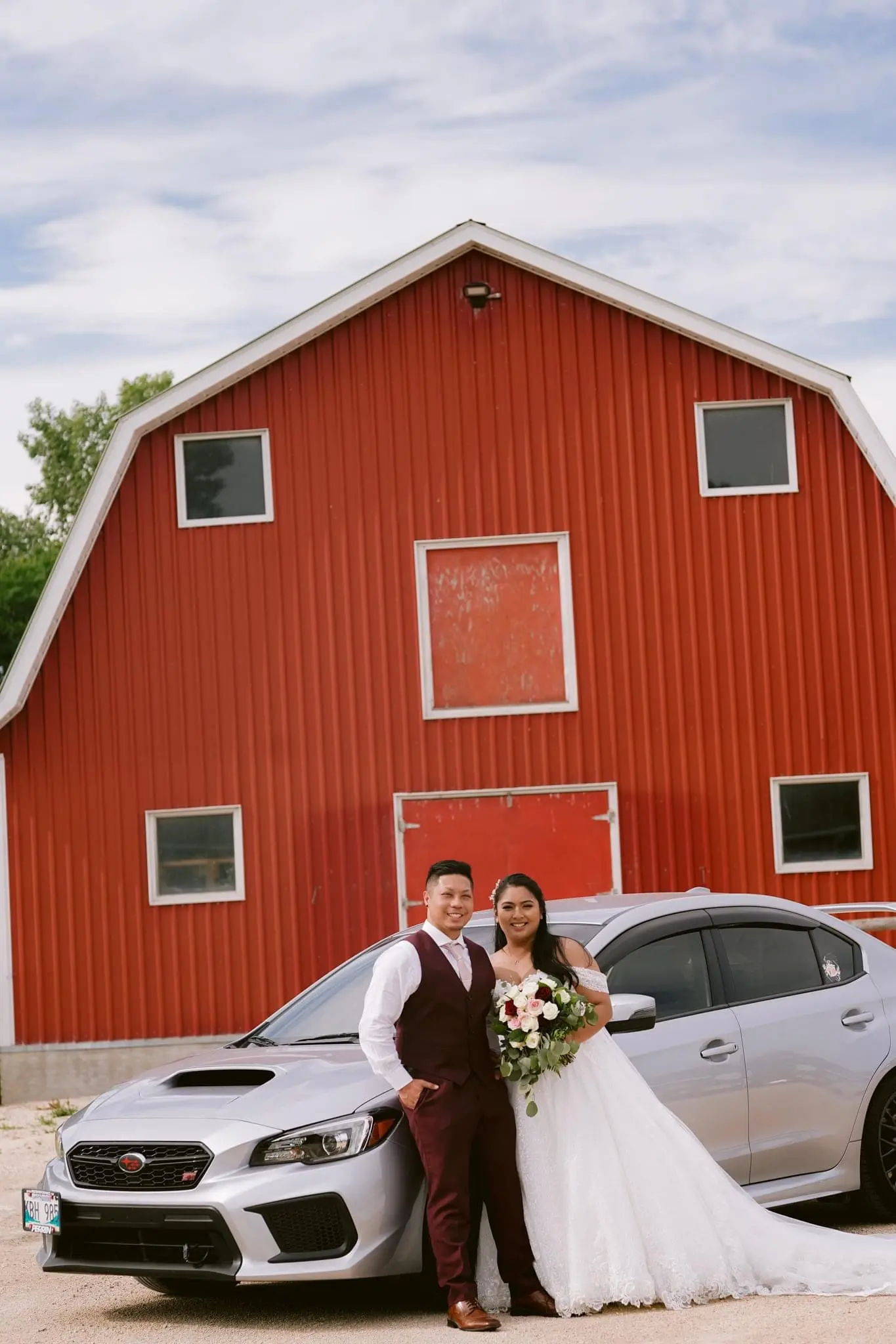 Bride and groom leaning on a silver sports car.