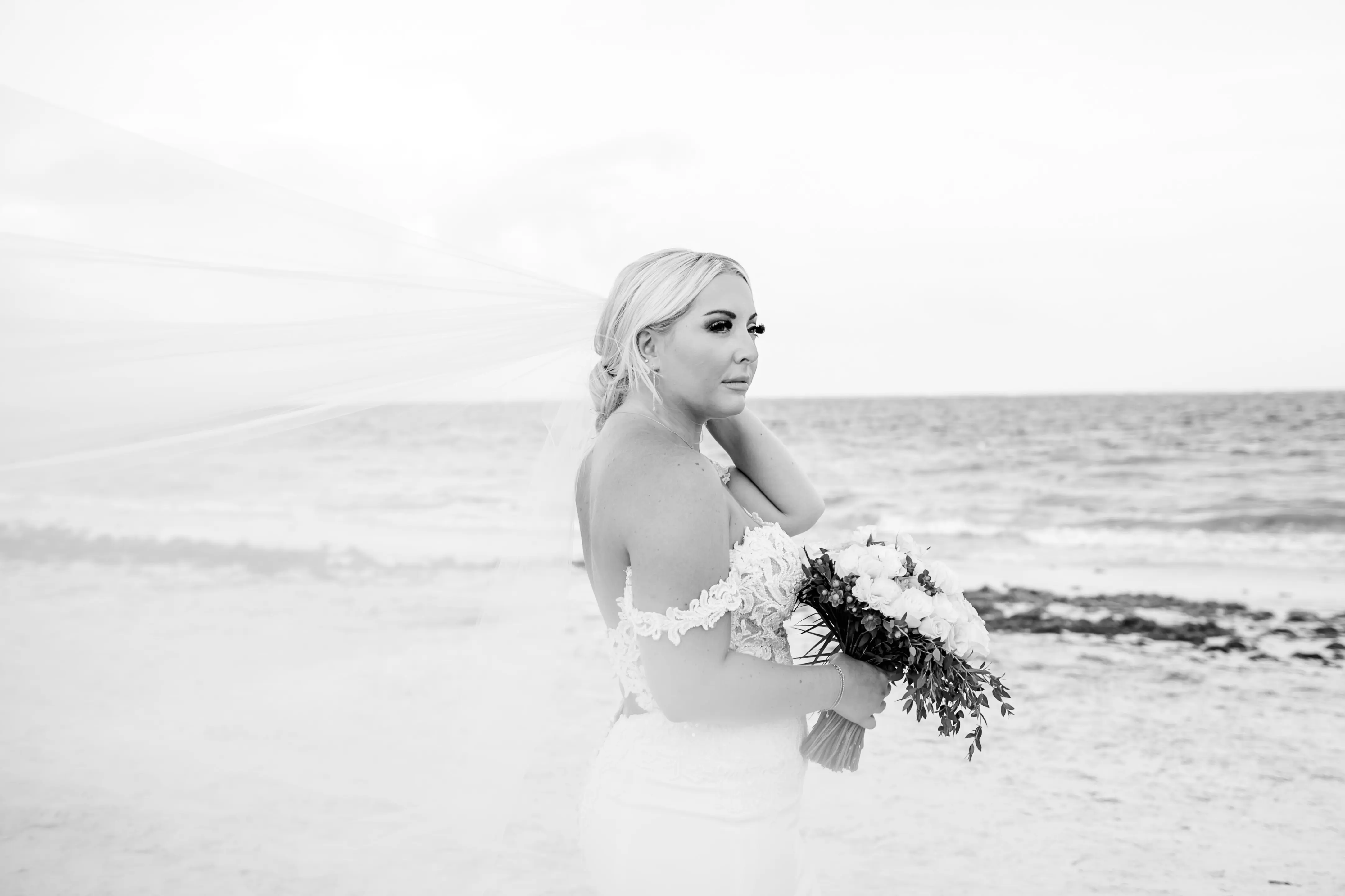 Bride stood by the shore with veil floating behind her.