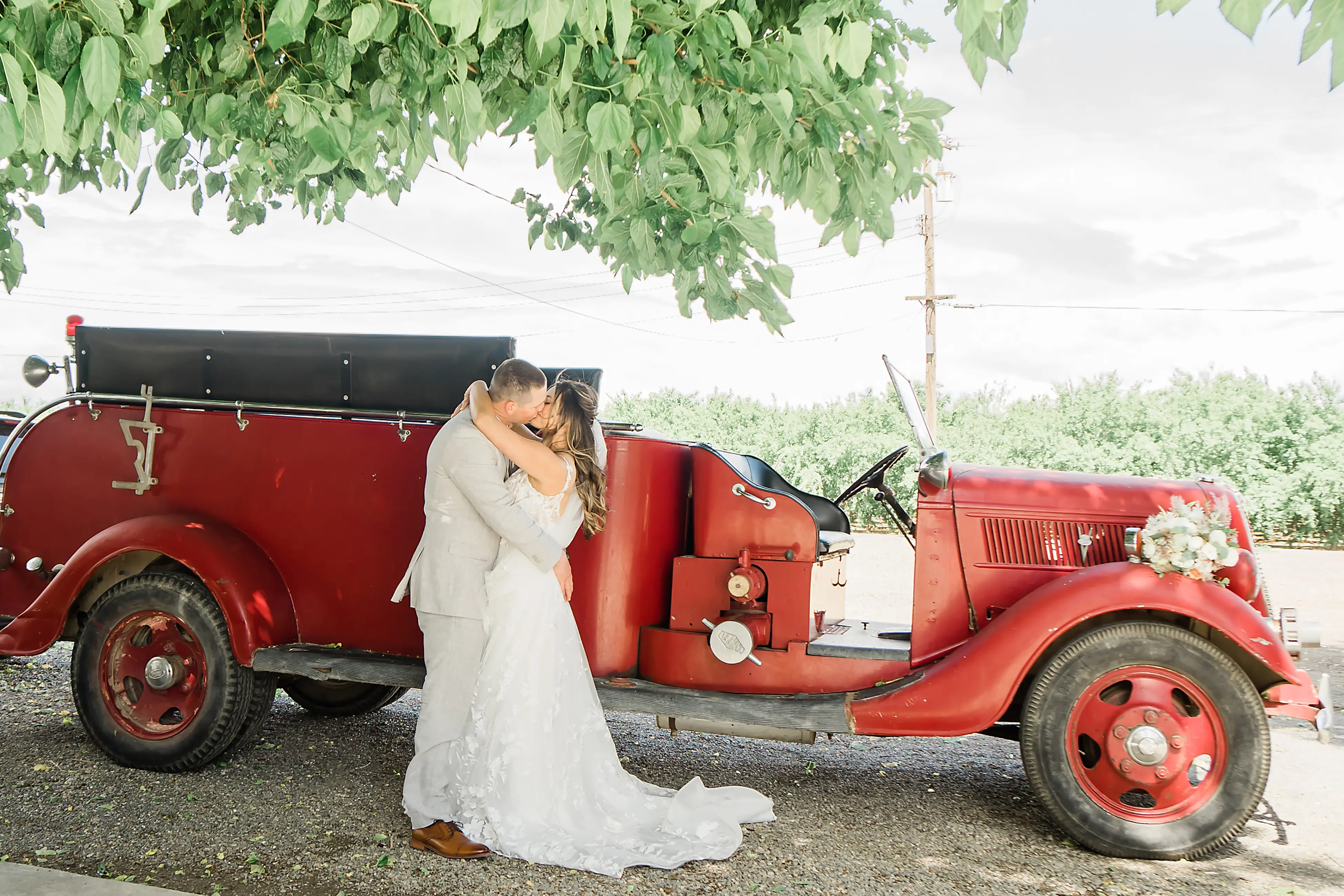Groom Kisses Bride In Front of Fire Truck Bride Wears Floral Whimsical Wedding Dress Winter by Maggie Sottero