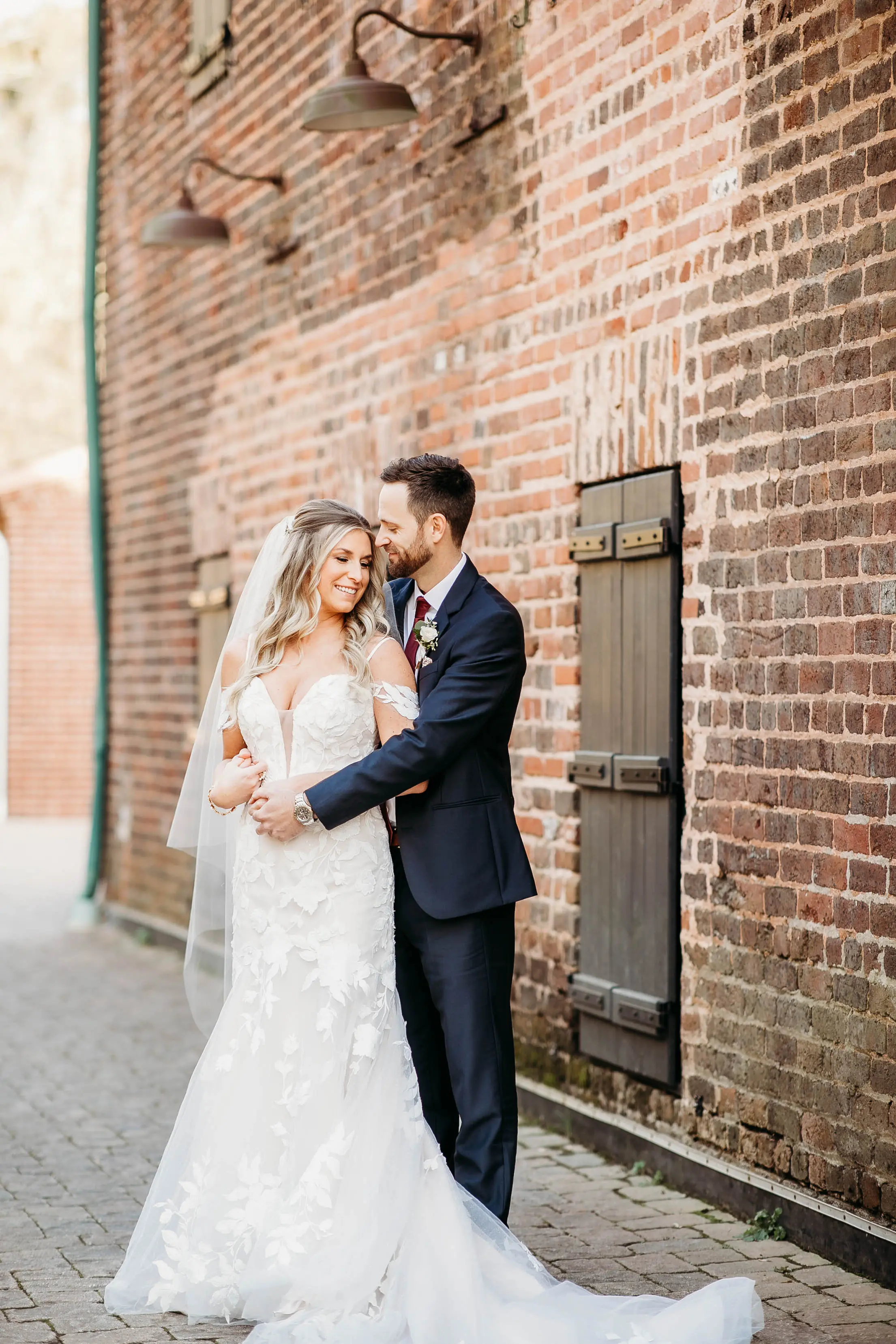 Bride And Groom Standing Together. Bride Wearing Mermaid Wedding Dress With Oversized Lace Called Hattie By Rebecca Ingram