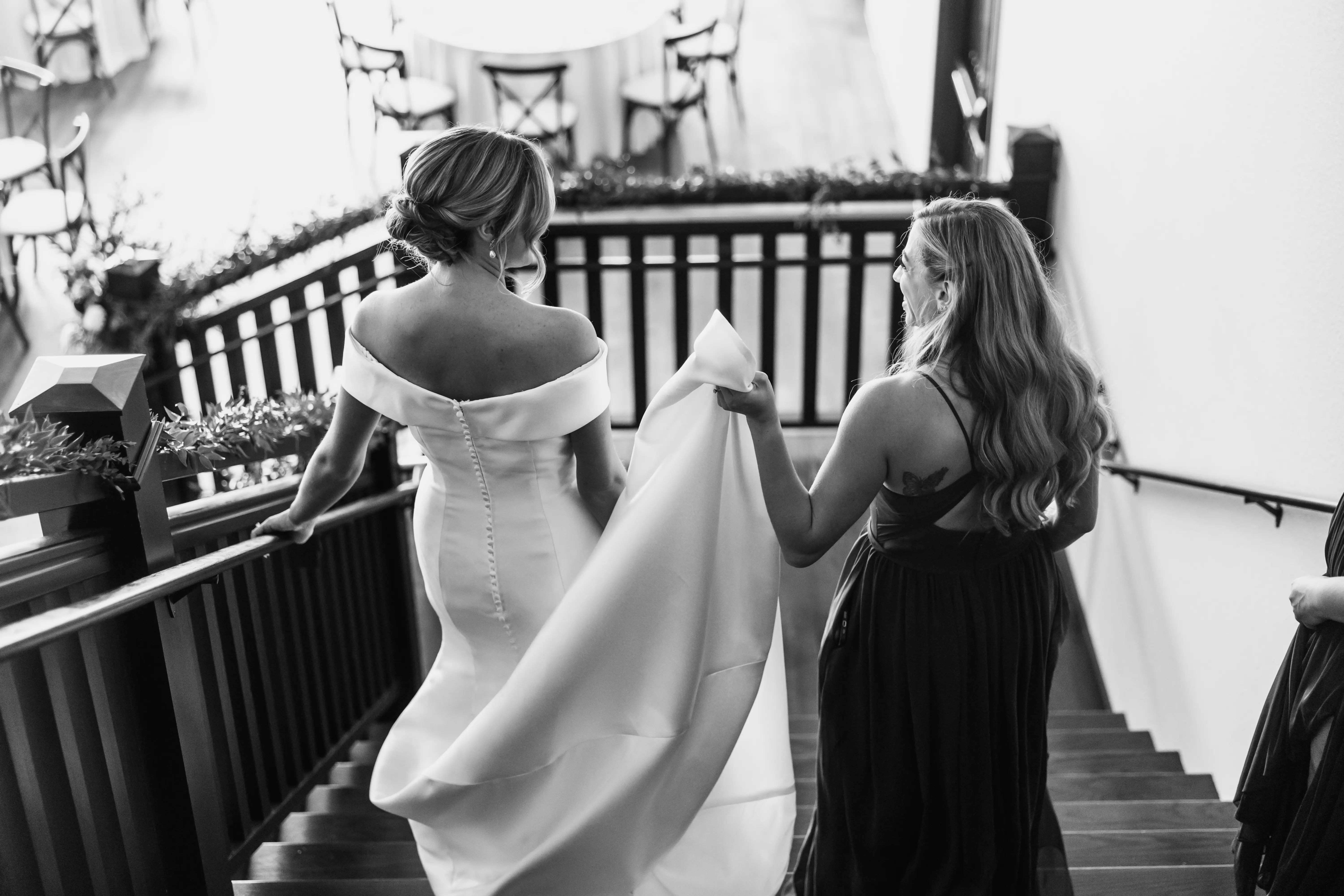 Bridesmaid Walking Down Stairs With Bride In Elegant Off The Shoulder Fit And Flare Wedding Dress Named Josie By Rebecca Ingram