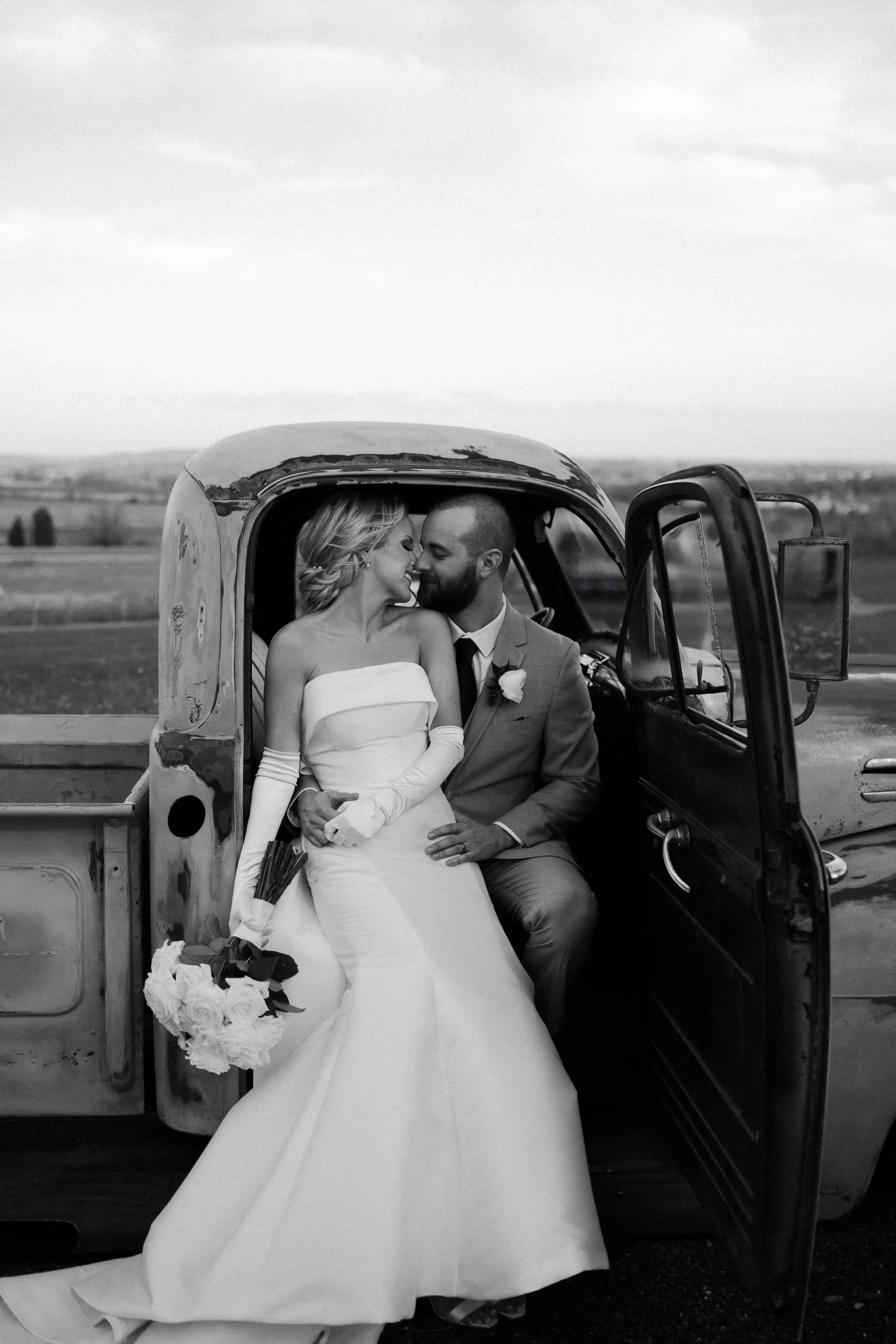 Groom Sitting In A Vintage Truck With Bride In A White Strapless Wedding Dress Named Mitchell By Maggie Sottero
