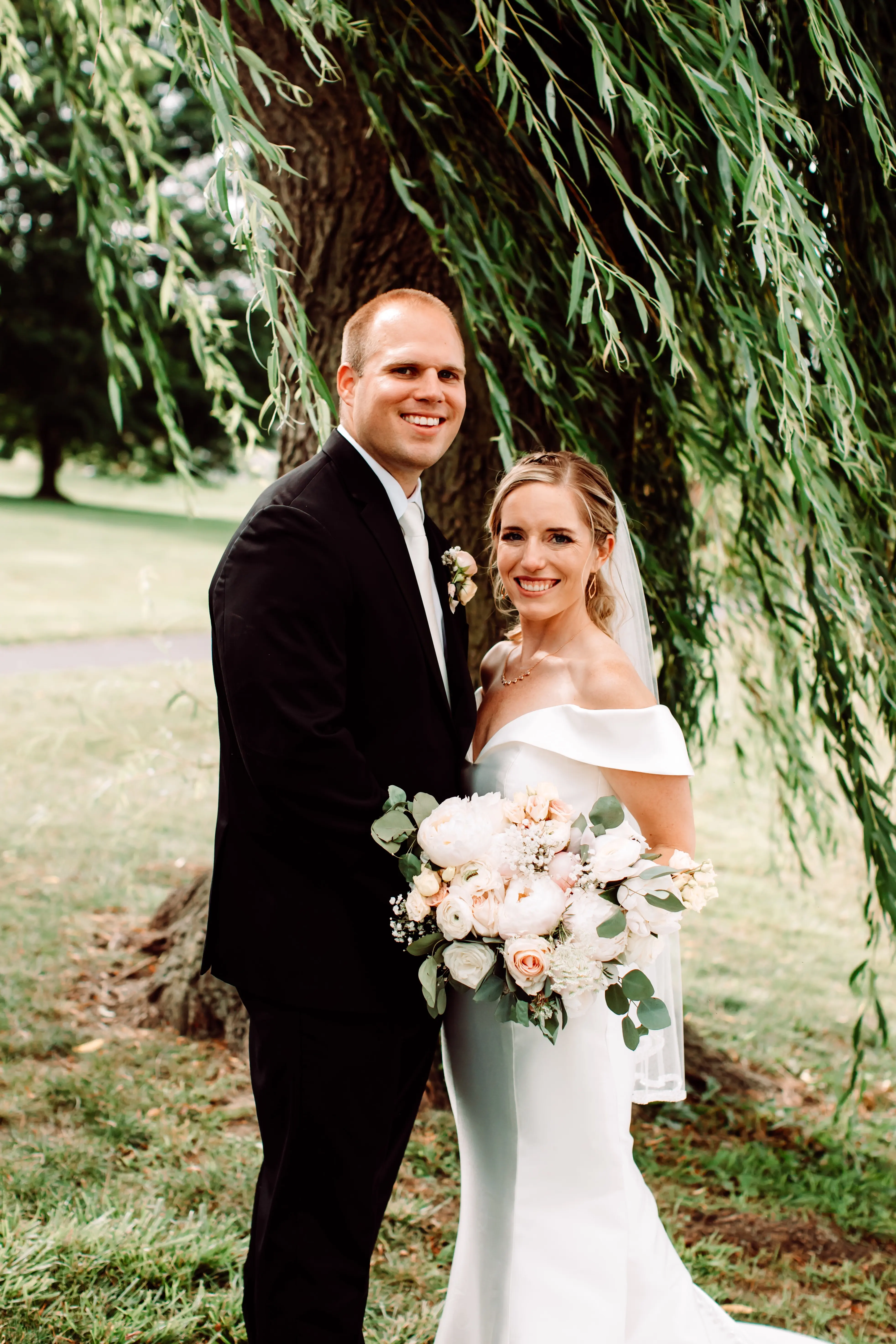 Bride and groom stood together the bride's bouquet is filled with peach peonies.