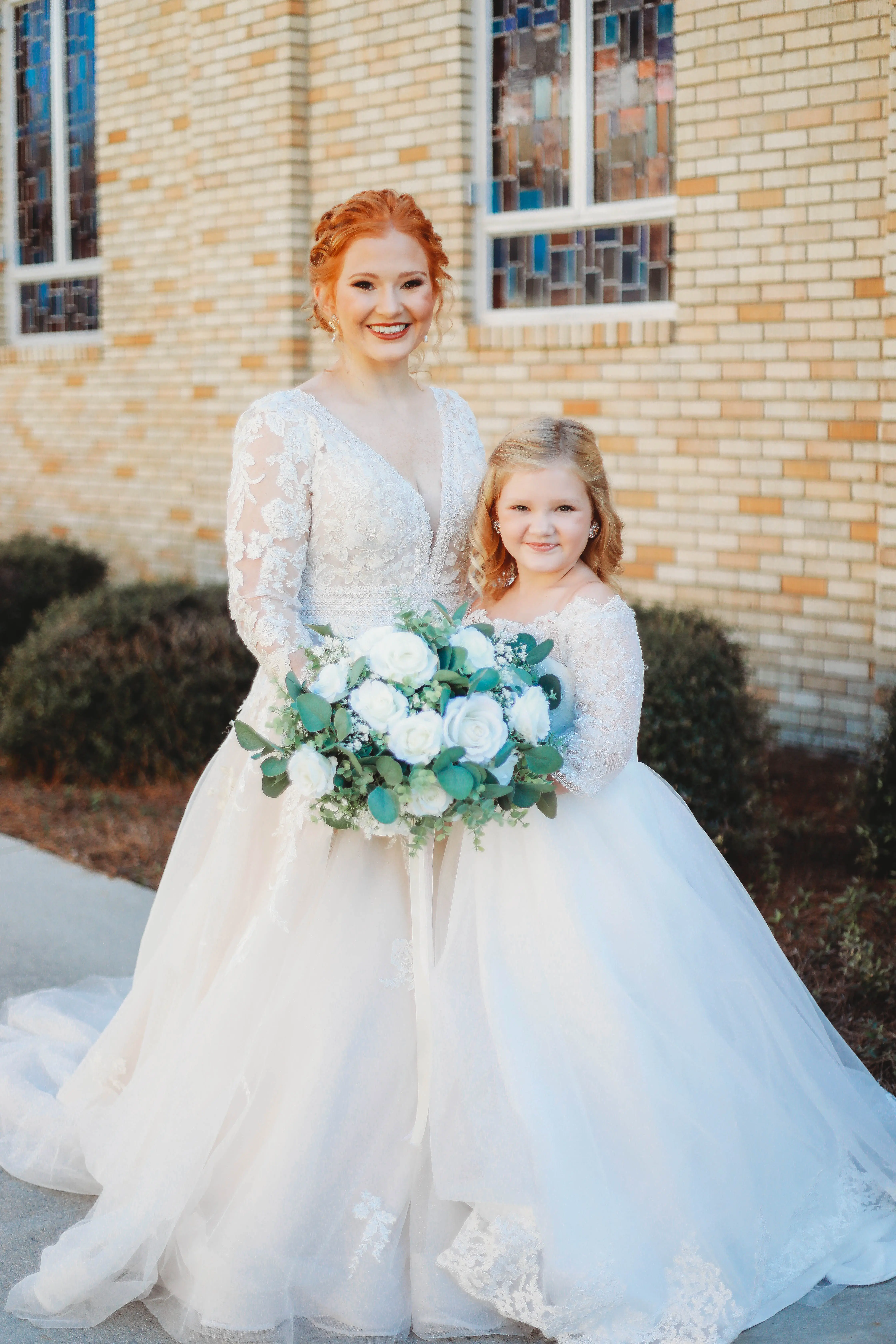 Bride Standing With Young Girl Wearing Similar White Gowns. Bride Wearing Illusion Sleeve A-line Wedding Dress Called Raphael By Maggie Sottero