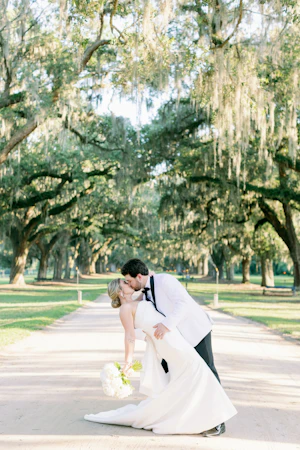 Bride with groom wearing strapless elegant mermaid wedding dress outdoors holding flower bouquet.