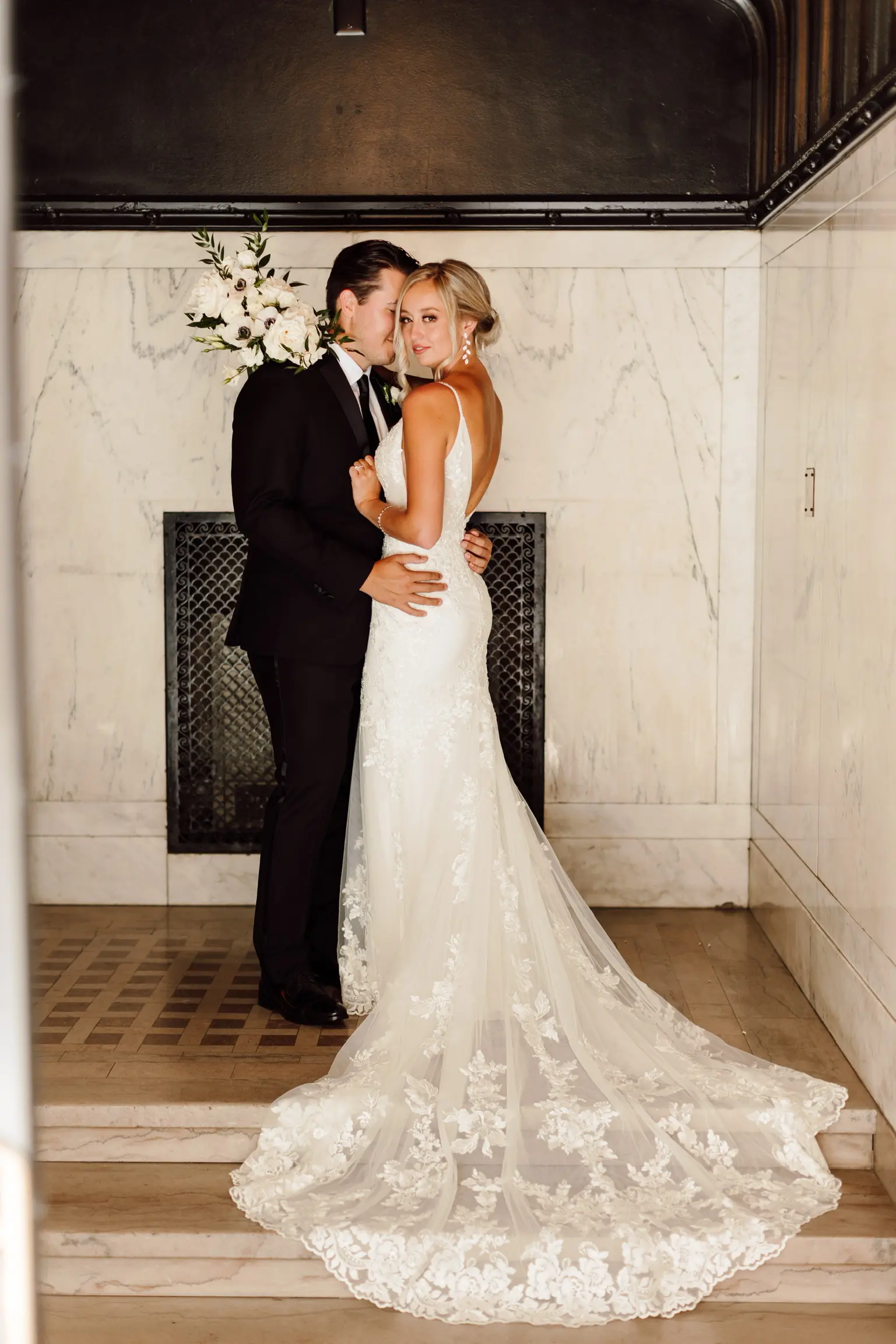 Bride Wearing Sparkle Lace Long Train Wedding Dress Called Fontaine By Maggie Sottero Held By Groom In Granite Staircase Looking Back