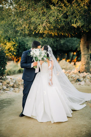 Bride Wearing Sexy Ballgown Wedding Dress Called Derrick By Maggie Sottero Kissing Groom Behind A Bouquet